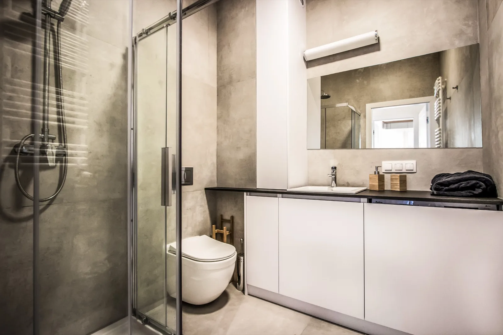 Bathroom full view with glass walk-in shower, wall-hung WC, white floating vanity with grey stone countertop, and concrete-effect wall tiles