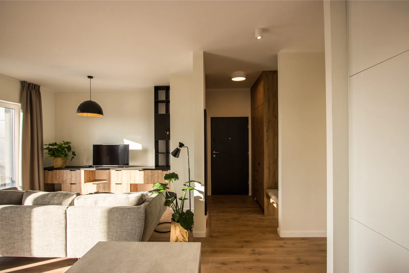 Dining and media wall panorama at dusk with warm pendant glow, oak table, and floor-to-ceiling custom shelving unit illuminated