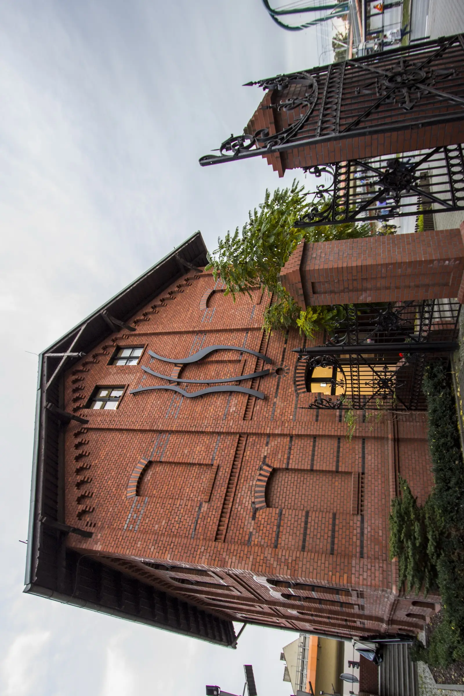 Exterior: preserved 1890 Carl Meyer red brick industrial facade with Neo-Romanesque decorative brickwork, arched window openings, climbing ivy, and heritage golden lantern fixture