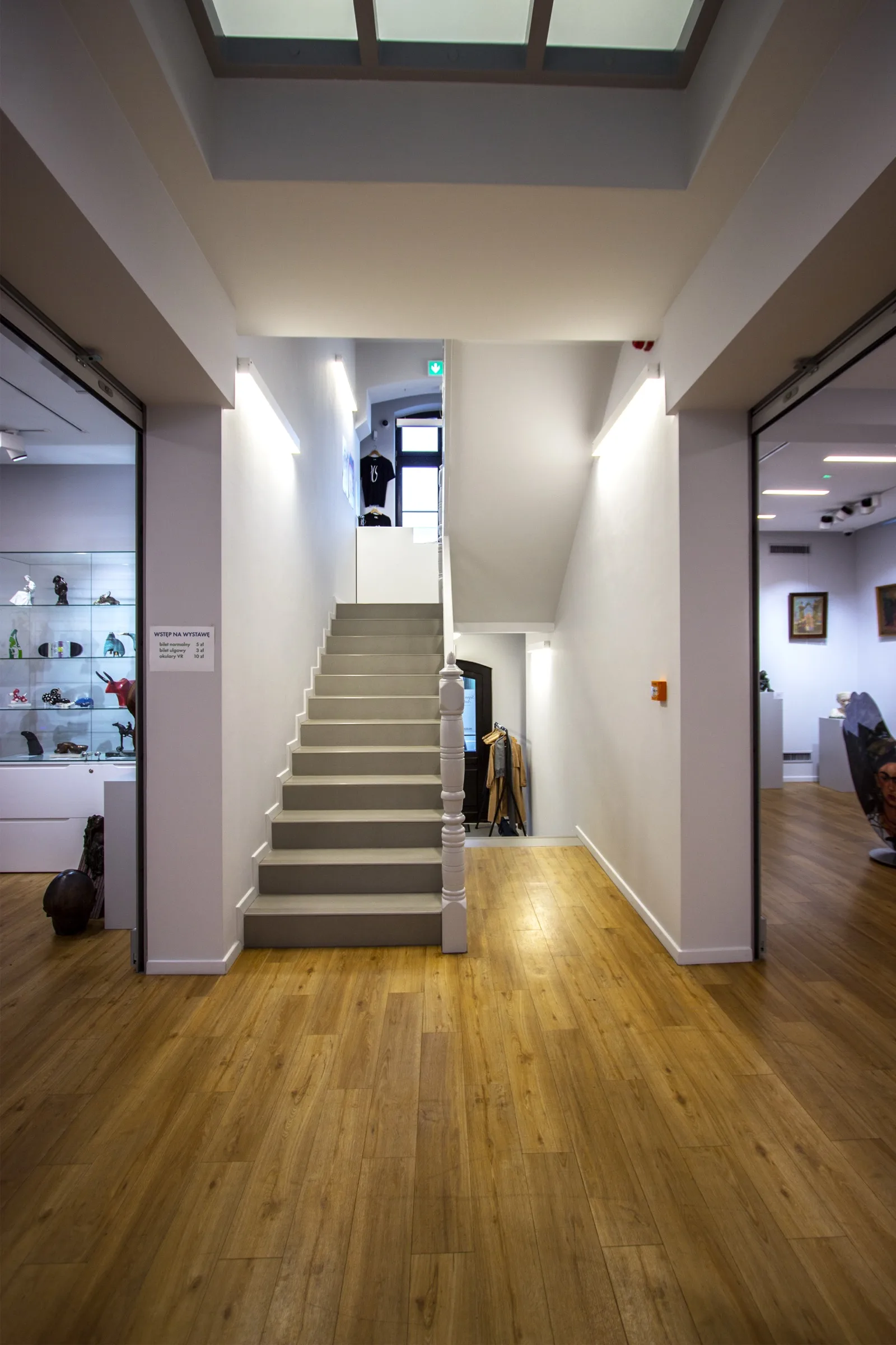 Interior: entry hall showing central staircase with modern white railings, decorative spherical metal node details, and skylight above flooding the adaptive reuse museum with natural light