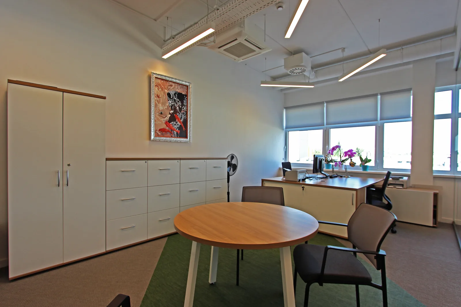 Director office storage and art detail showing built-in white cabinetry, framed artwork, and the refined white-on-white interior with warm wood accents