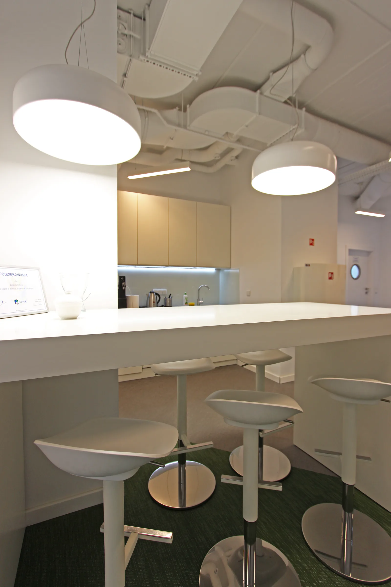 Kitchen area close-up with bar stools, pendant lights, natural wood surface finishes, and the warm breakout atmosphere within the corporate environment