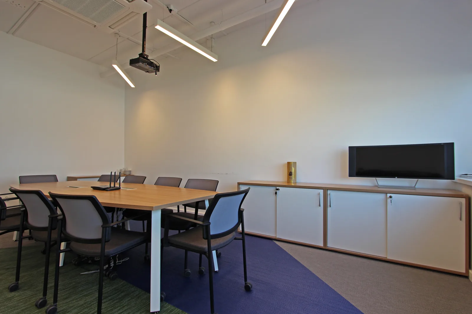 Conference room with ceiling-mounted projector, white furniture, glass partitions, and the clean corporate aesthetic against the matte black exposed ceiling