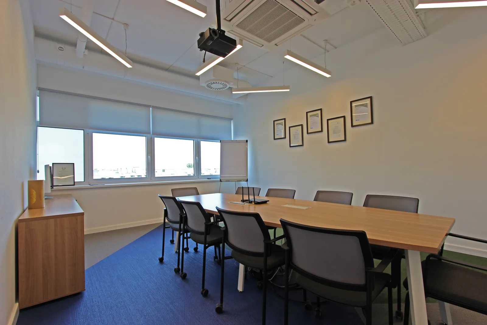 Kitchen and breakout area with pendant lighting, natural wood round tables, bar stools, and the warm contrast against the otherwise minimal office palette