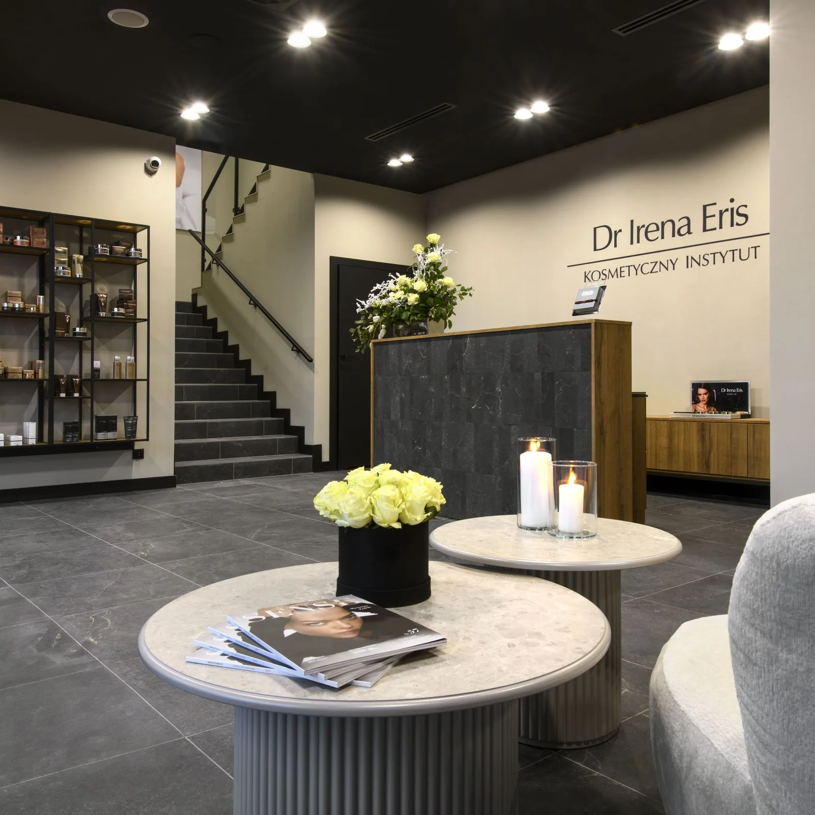 Interior: reception and waiting area of Dr Irena Eris beauty salon with graphite-painted walls, suspended ceiling with built-in lighting, and glass partition separating hair salon zone