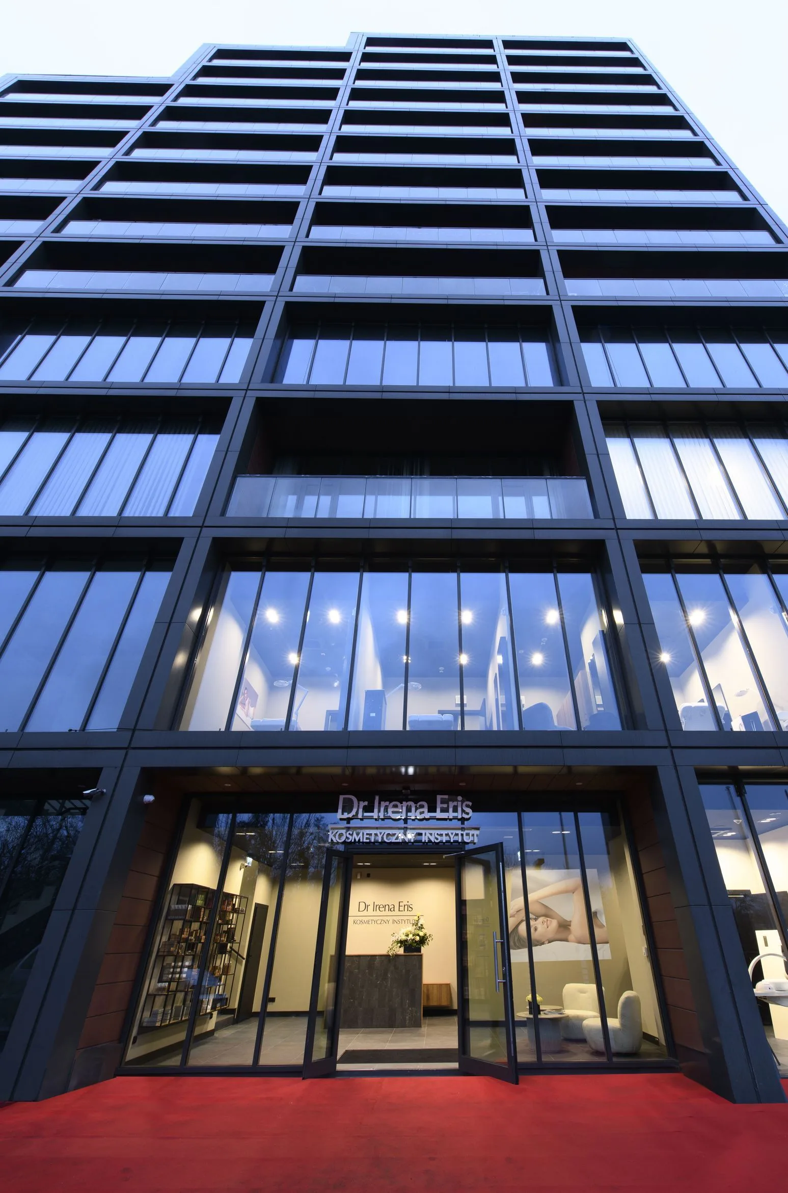 Interior: vertical view of Dr Irena Eris salon showing spatial depth through glass partition, graphite walls, and consistent material palette from reception to treatment zones