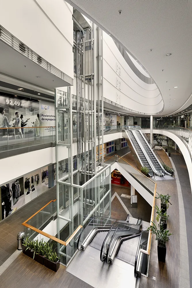 Interior: portrait photograph of Drukarnia Mall vertical circulation zone showing escalator and multi-level atrium view