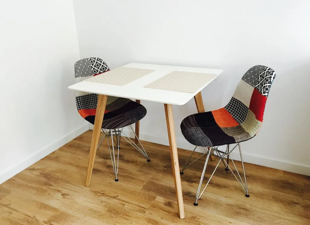 Residential furniture detail with white table and patchwork Eames-style chairs, oak laminate floor, white walls