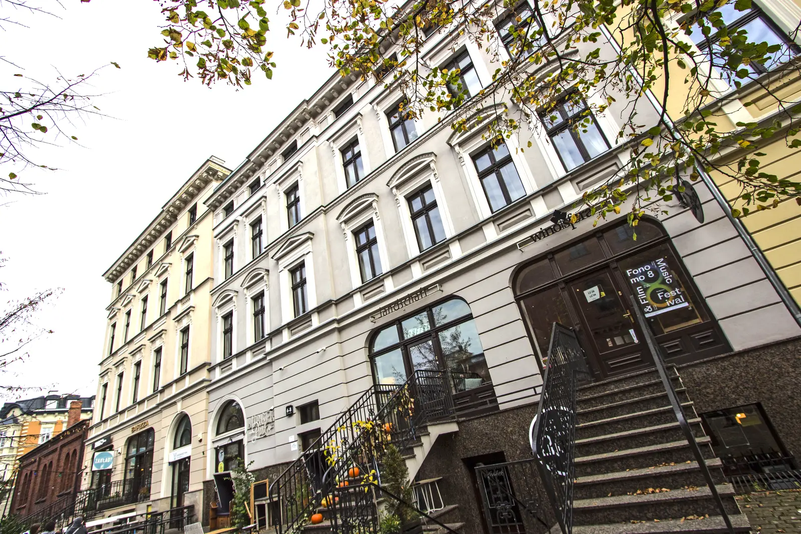 Autumn full facade with Forme and Fest signage, mature trees with yellow leaves, overcast sky, restored upper floors with ornamental cornices