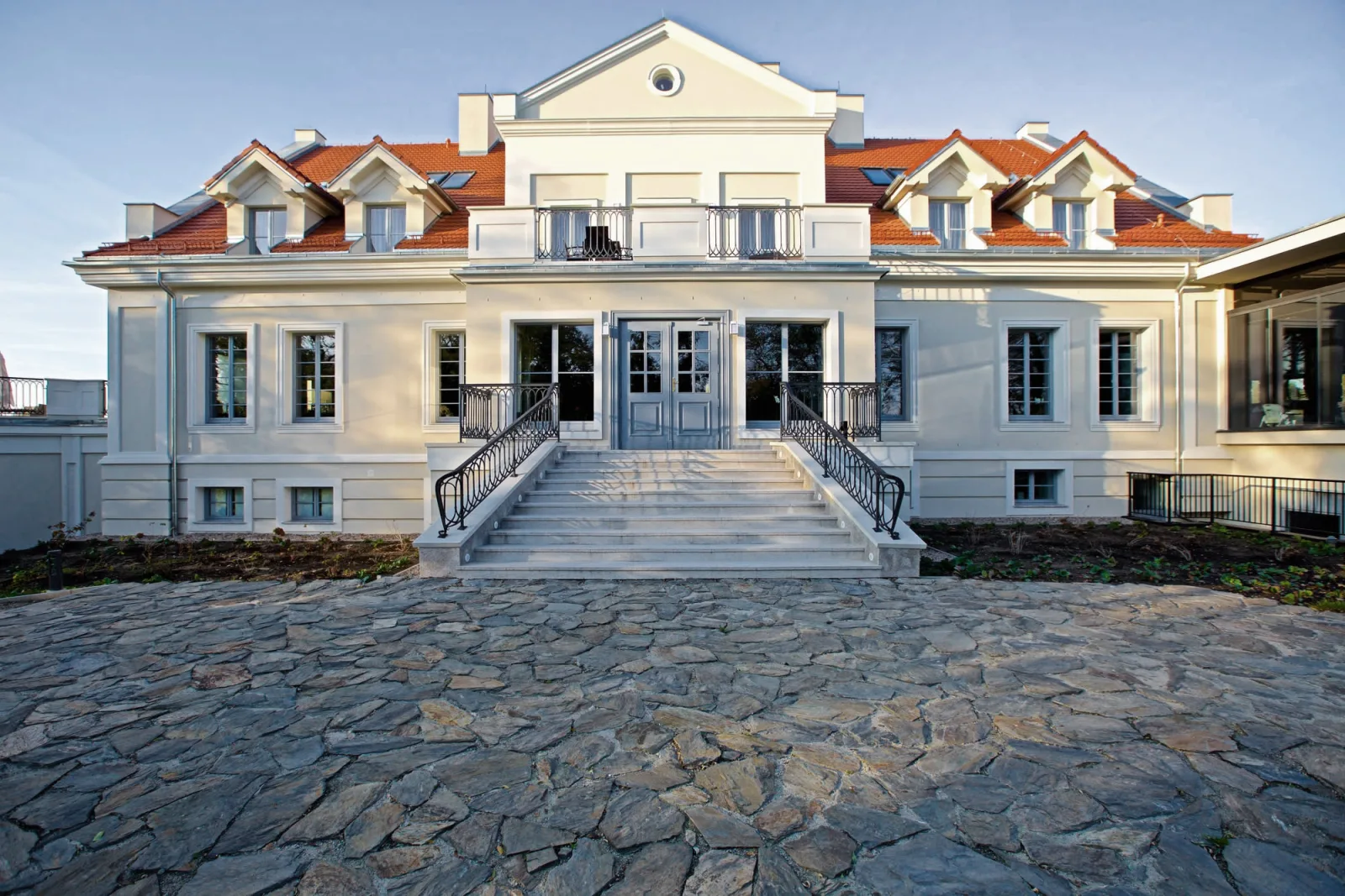 Main entrance with cobblestone forecourt, stone steps, wrought iron railings, and the heritage portico of the Old Manor