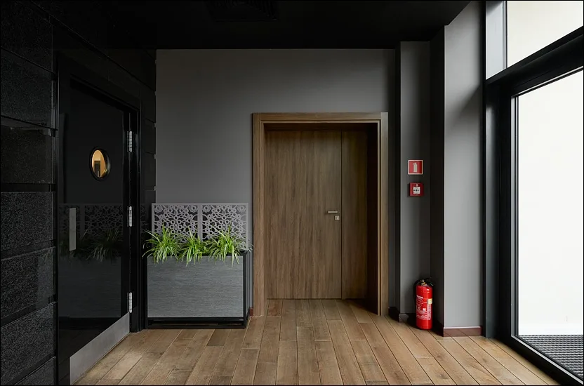 Hotel corridor with walnut door, botanical screen partition, and oak flooring