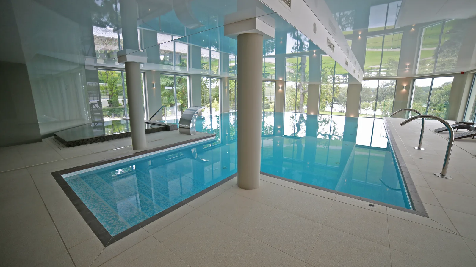 Infinity pool angle showing wide view with mosaic tiles, waterfall feature, glass walls, and parkland panorama