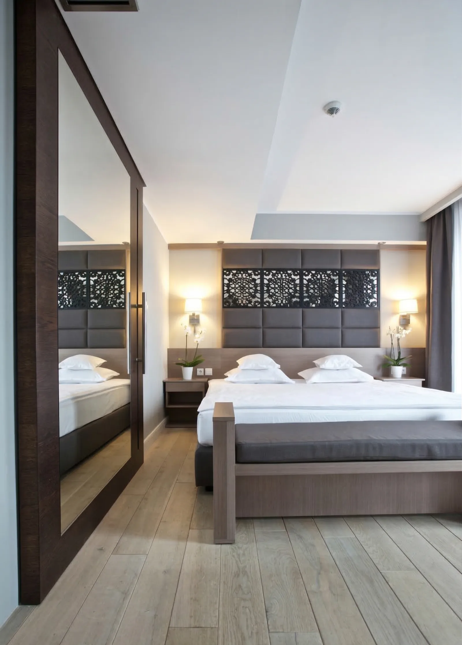 Guest room with botanical perforated headboard, mirror wardrobe, and oak herringbone floor