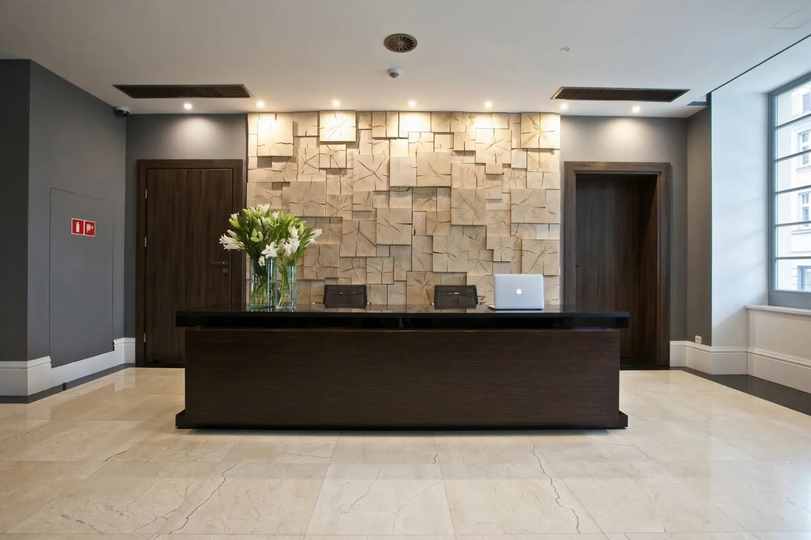 Reception desk with 3D wood block wall treatment, dark walnut desk, travertine floor, and white lilies