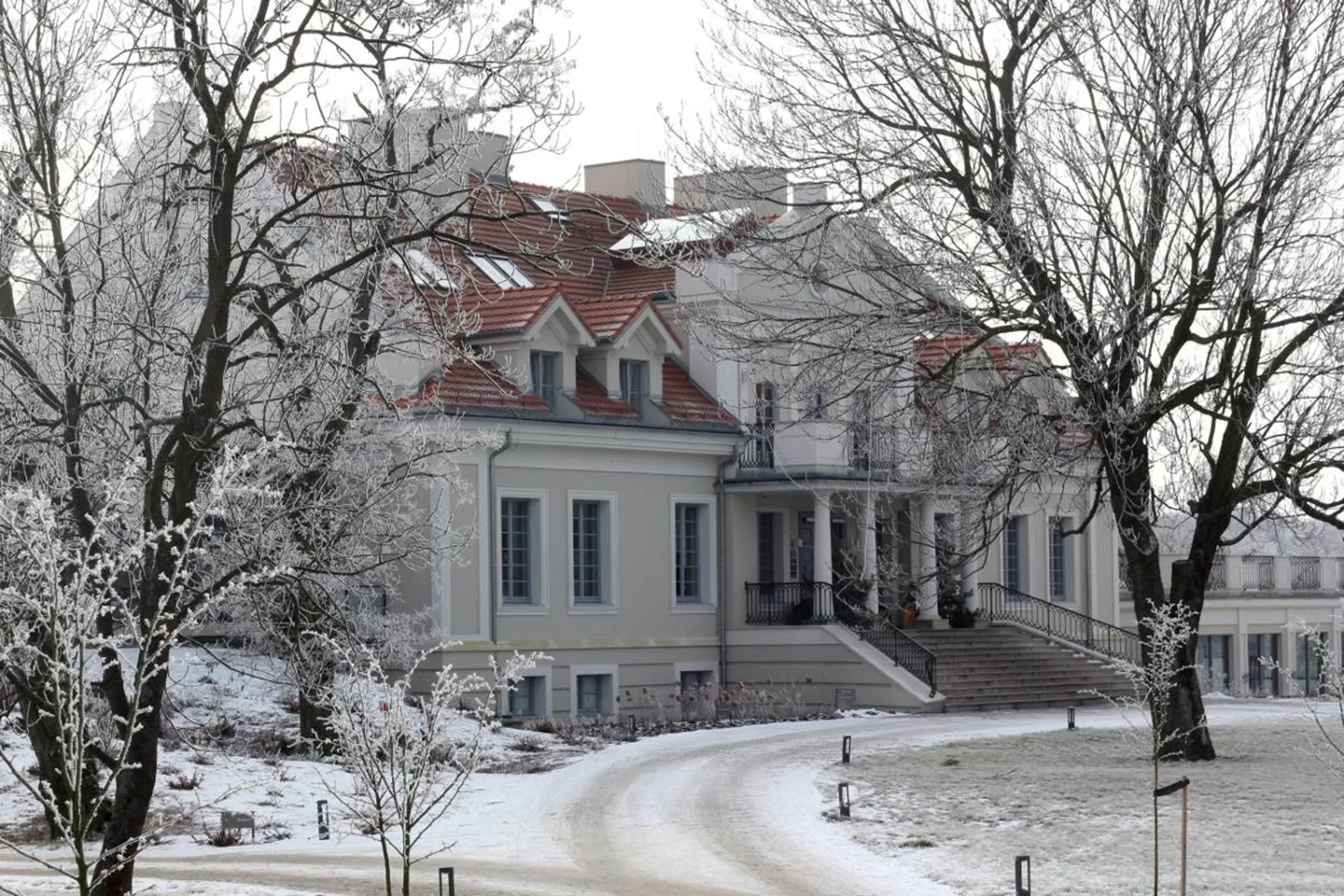 Winter exterior with Old Manor in snow, frosted trees, and red tile roof against grey sky