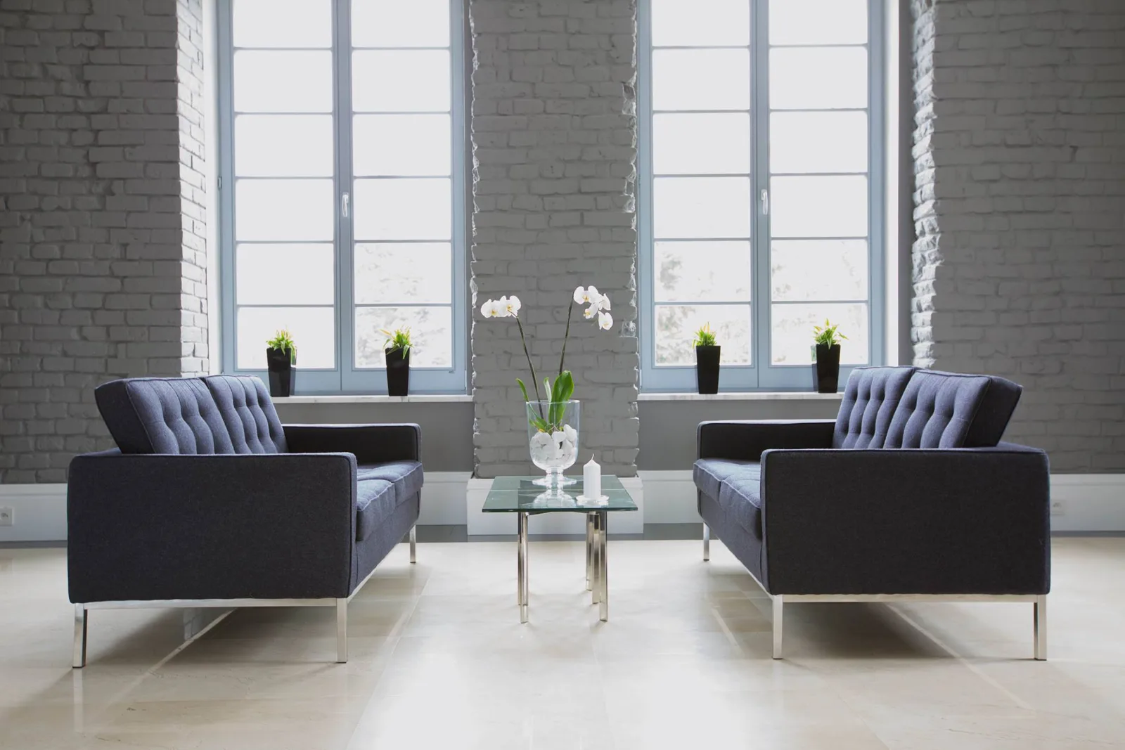Lounge with Florence Knoll sofas, exposed brick walls, glass coffee table, and orchid styling