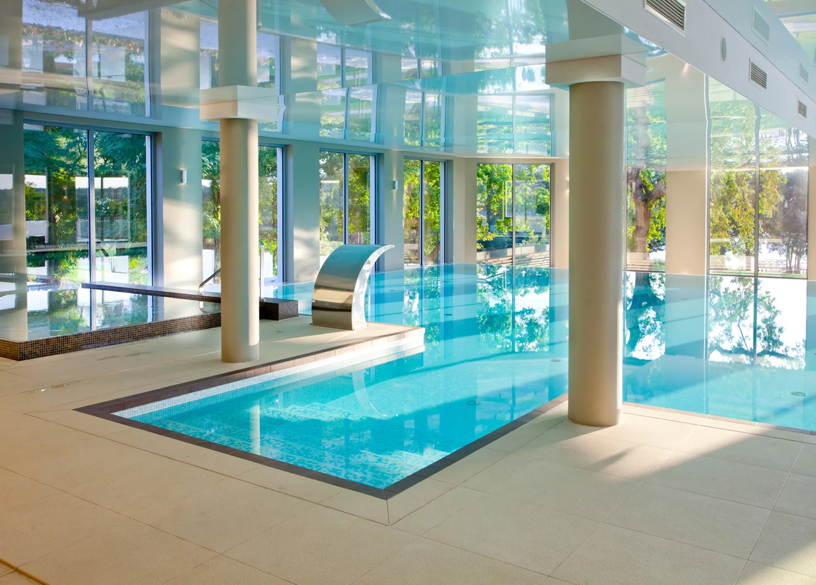 Infinity pool wide angle with mosaic tiles, waterfall feature, stretch ceiling, and loungers overlooking the parkland