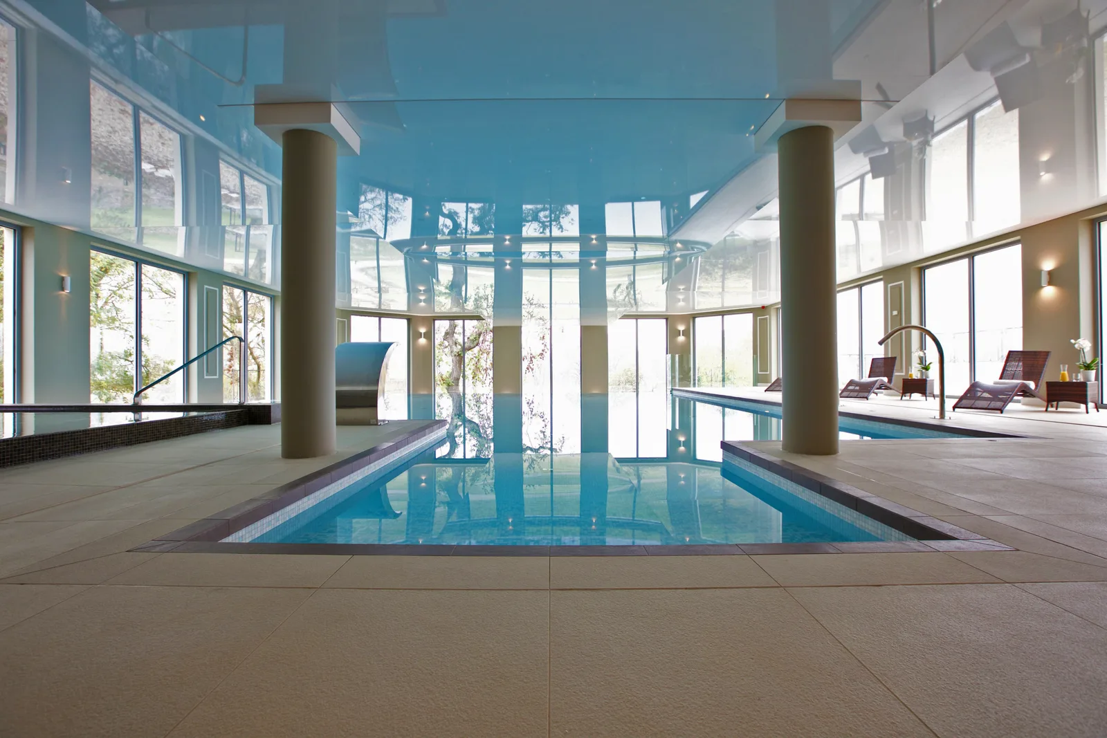 Infinity pool with stretch ceiling creating turquoise reflections, columns framing the landscape view beyond