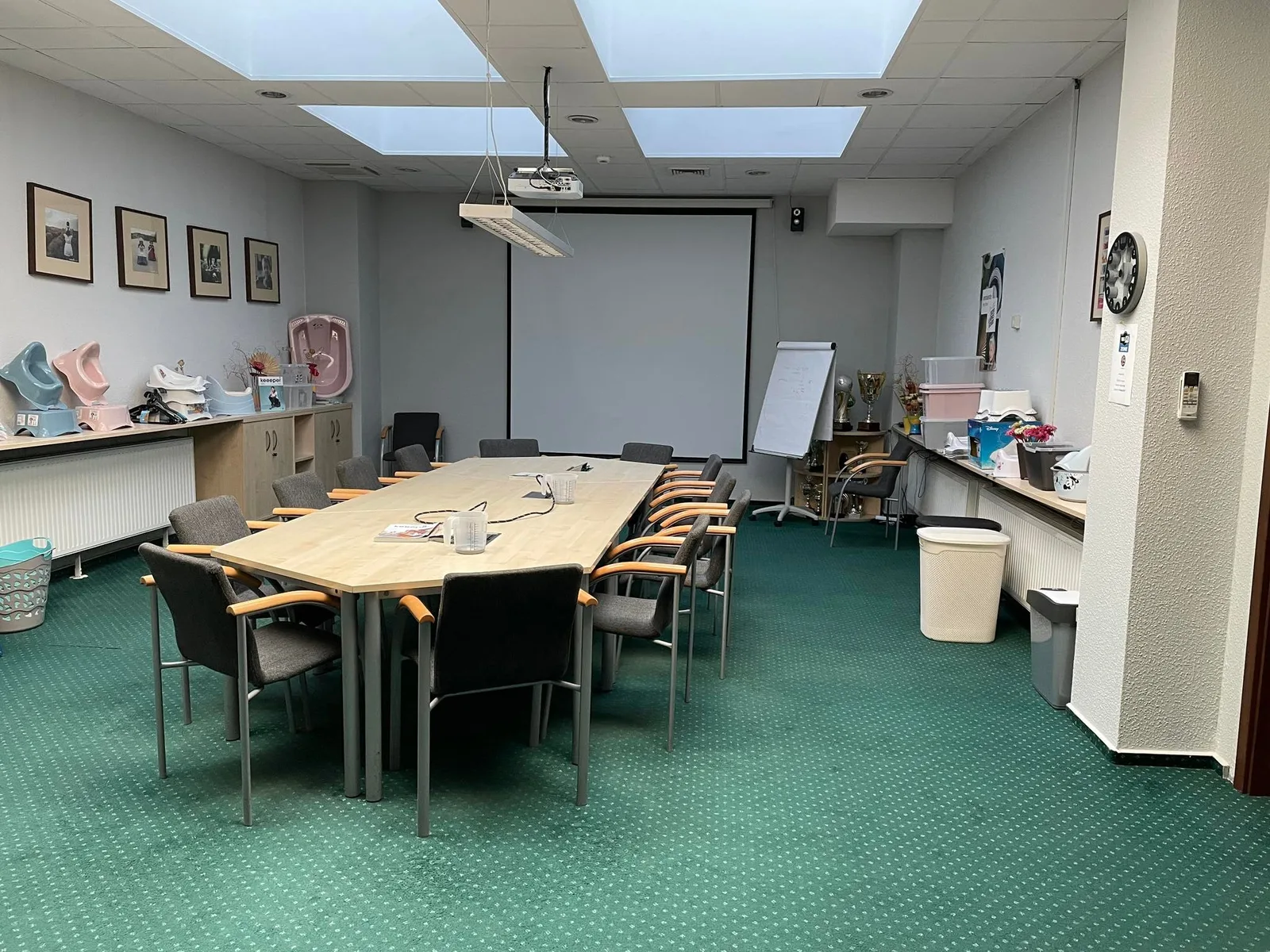 Pre-renovation conference room photo with dated green carpet, old ceiling tiles, basic furniture, and keeeper product samples on shelves