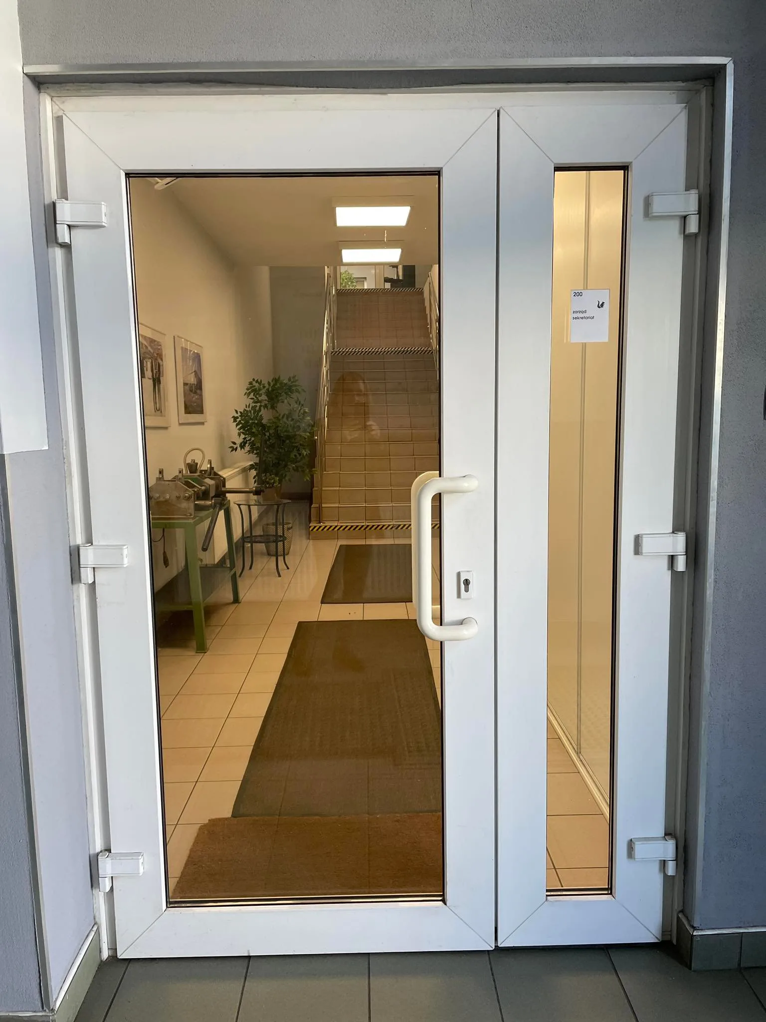 Pre-renovation executive office photo with existing furniture, dated wall finishes, green carpet flooring, and standard commercial window blinds