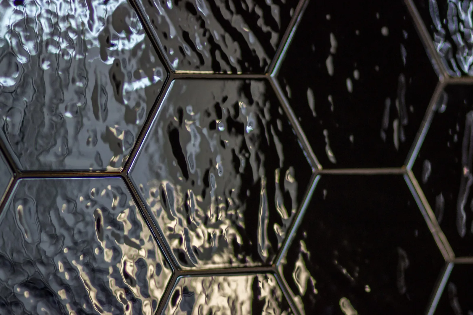 Detail: black hexagonal gloss tiles extreme close-up showing koi-scale rippled texture and glossy reflective surface