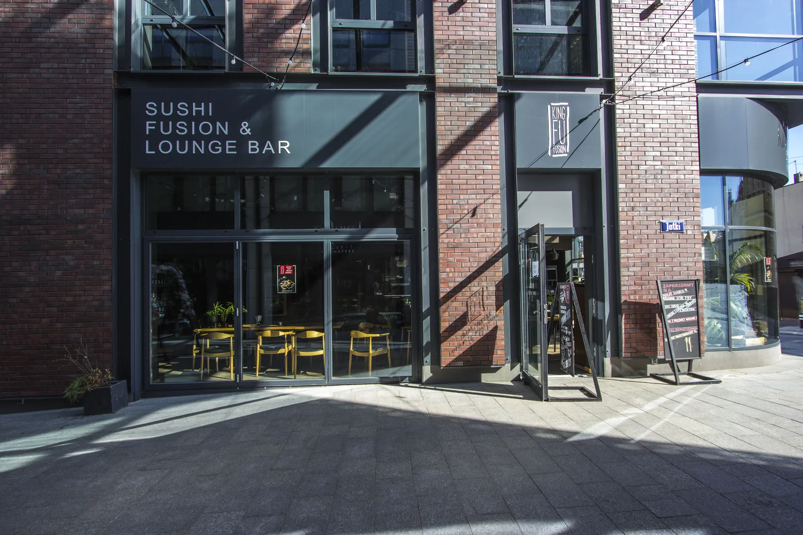 Exterior: street level with Sushi Fusion and Lounge Bar signage, outdoor terrace with yellow chairs, and A-frame menu board