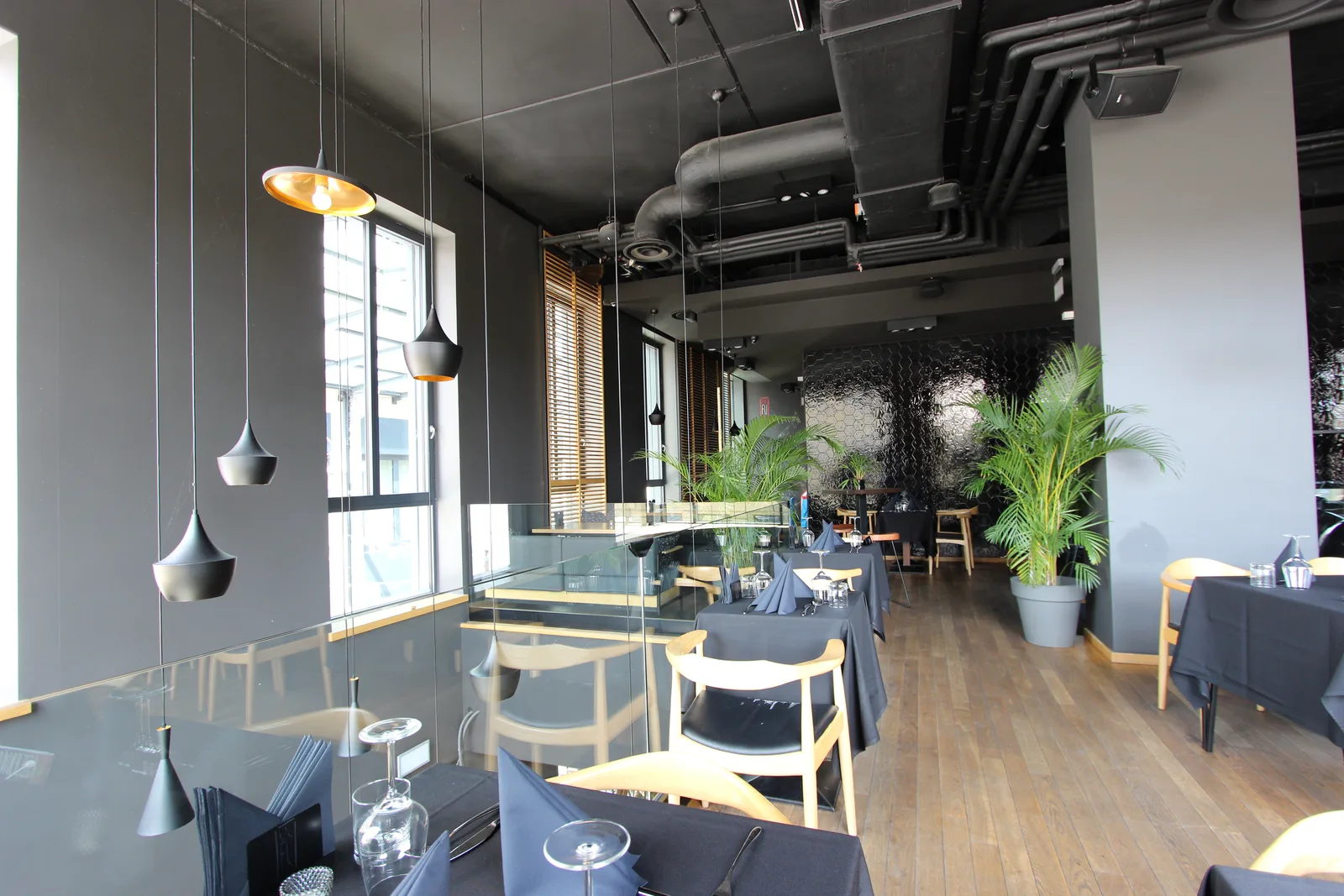 Interior: upper floor dining with pendants, full-height windows, glass balustrade to void, palm plants, and hexagonal tile feature wall