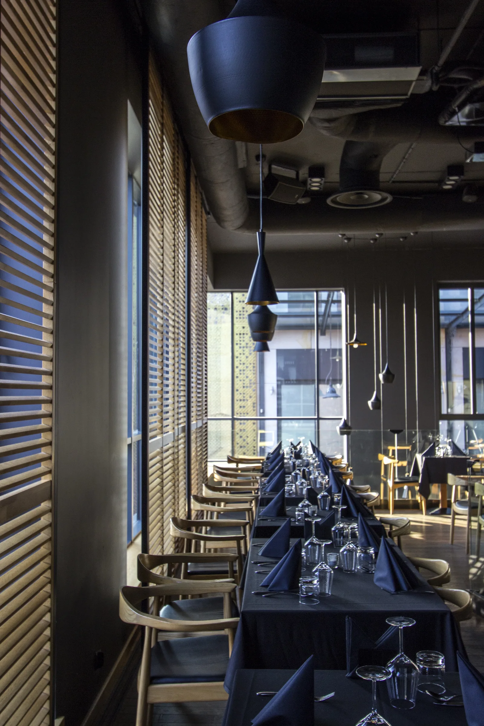 Interior: upper floor long table with row of oak chairs along venetian blinds and Tom Dixon pendants above