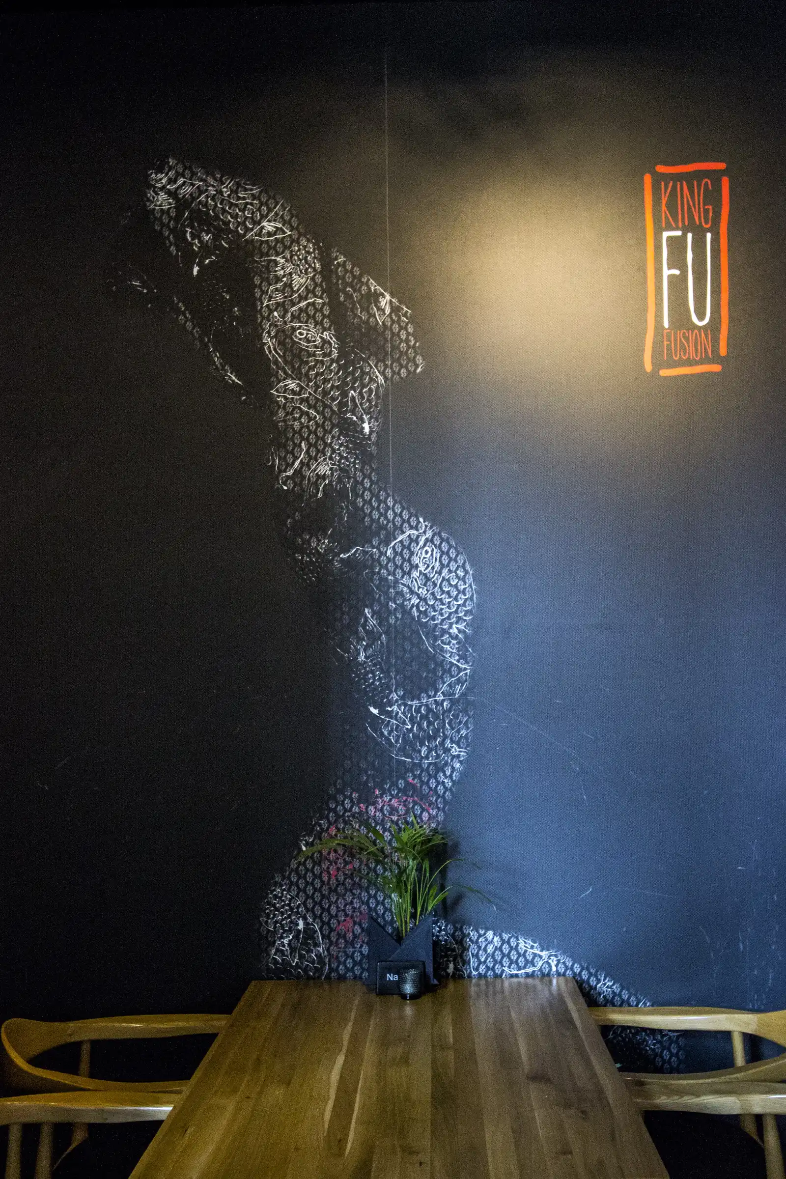 Interior: warrior mural with King Fu neon sign, wire mesh warrior figure, King Fu Fusion neon text, and oak tables below