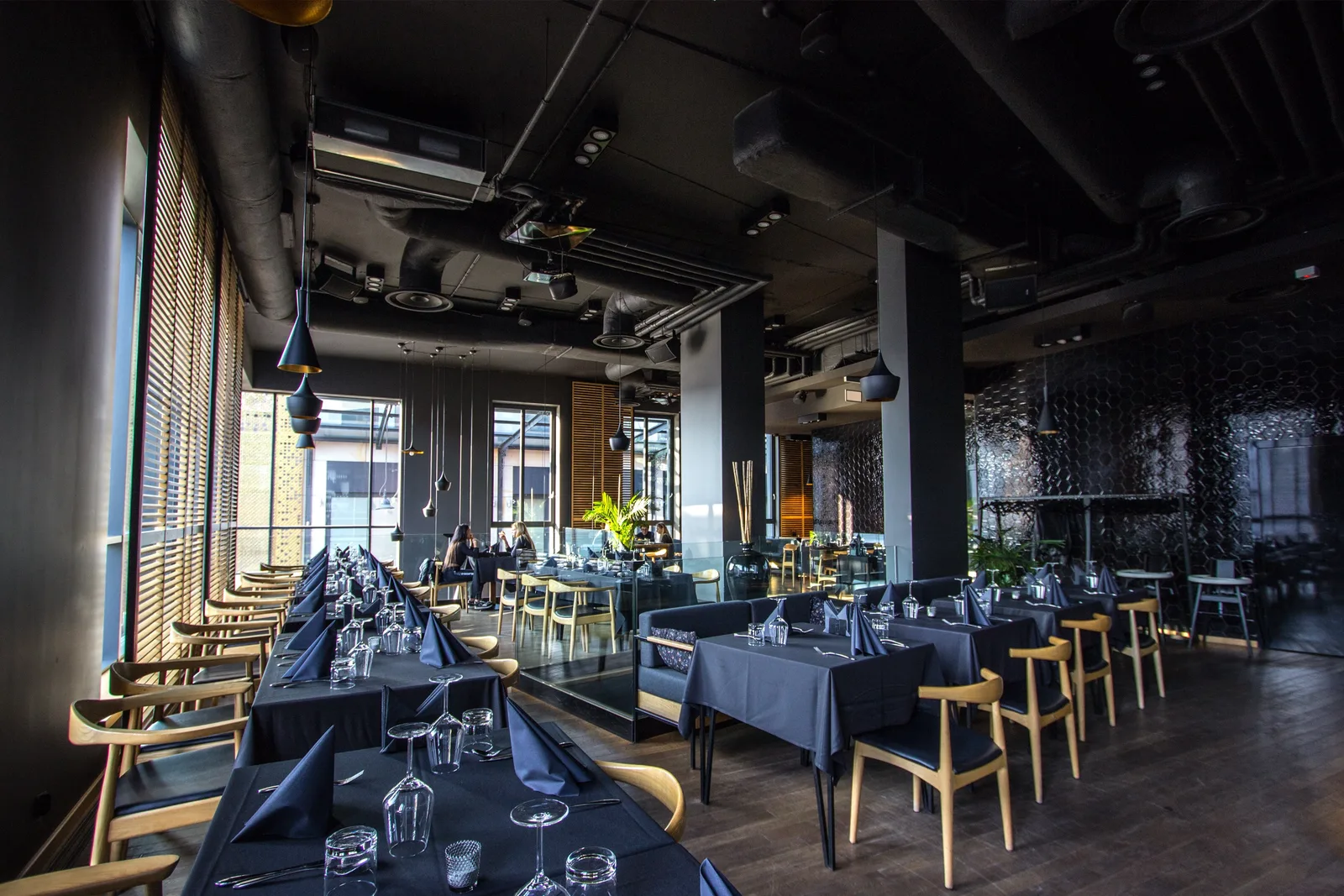 Interior: upper floor panoramic wide shot showing full dining space with dark oak flooring, black ceiling, venetian blinds, Tom Dixon pendants, and hexagonal tile wall