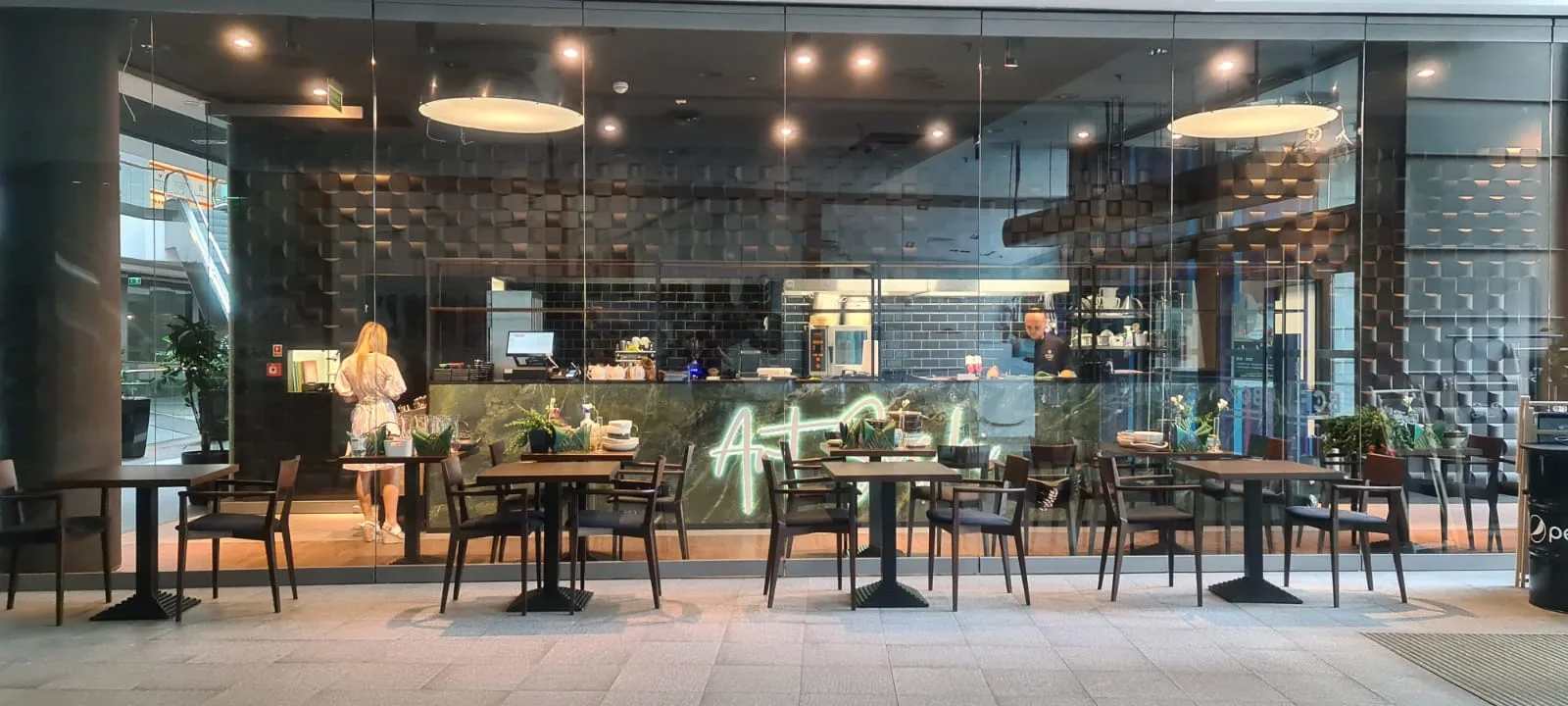 Exterior: through-glass photograph of the built restaurant showing Verde Karzai marble bar with green Art Sushi neon signage, 3D Decus Bent sculptural walls, Fameg walnut chairs, and staff behind the open sushi counter