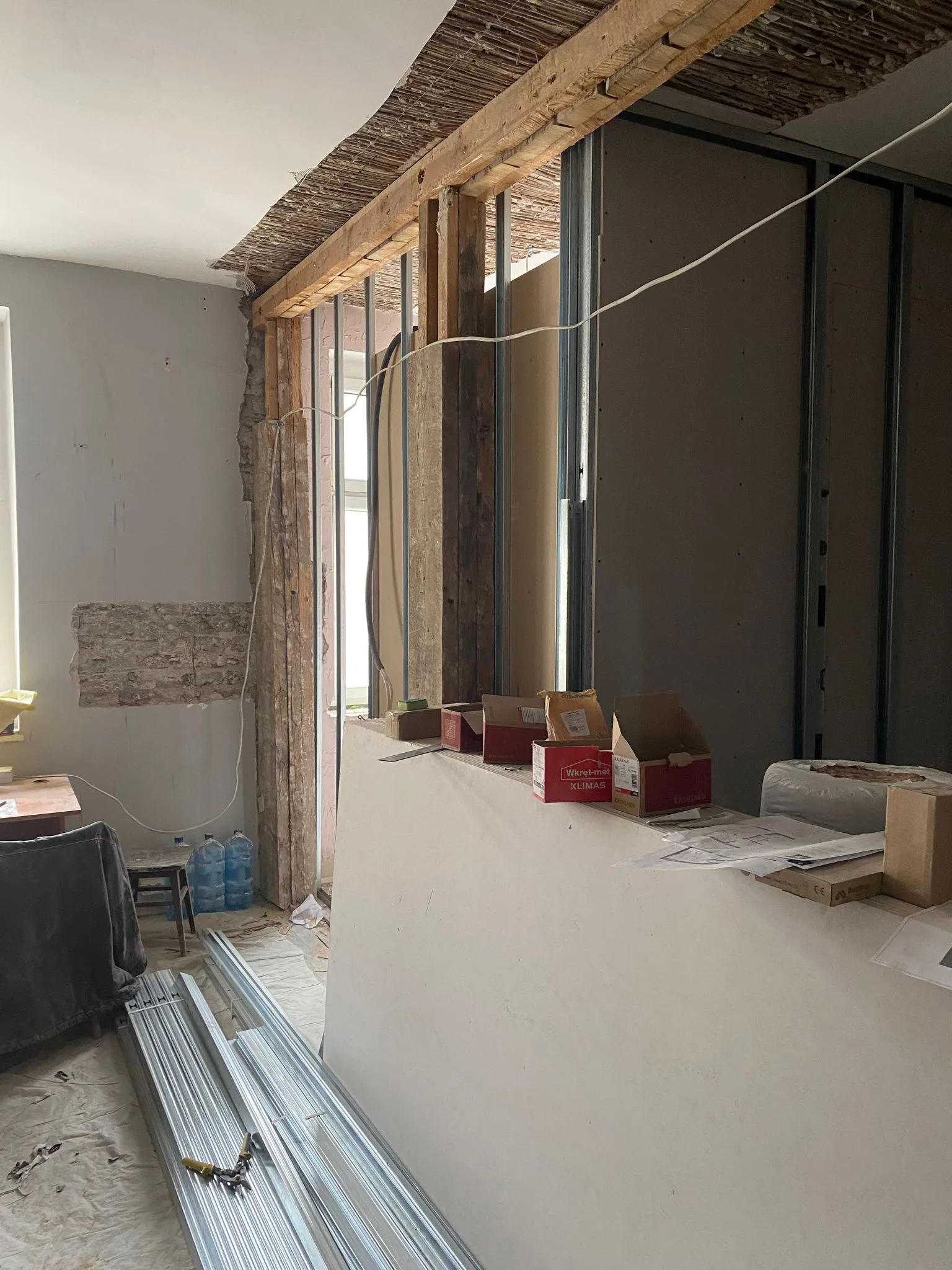 Construction: drywall partitions being installed with steel framing visible, materials staged on site, and temporary construction lighting in July 2023