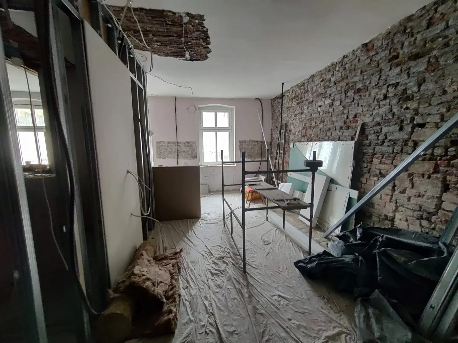 Construction: metal stud wall framing erected showing new apartment partition layout with electrical conduit runs and window openings in background