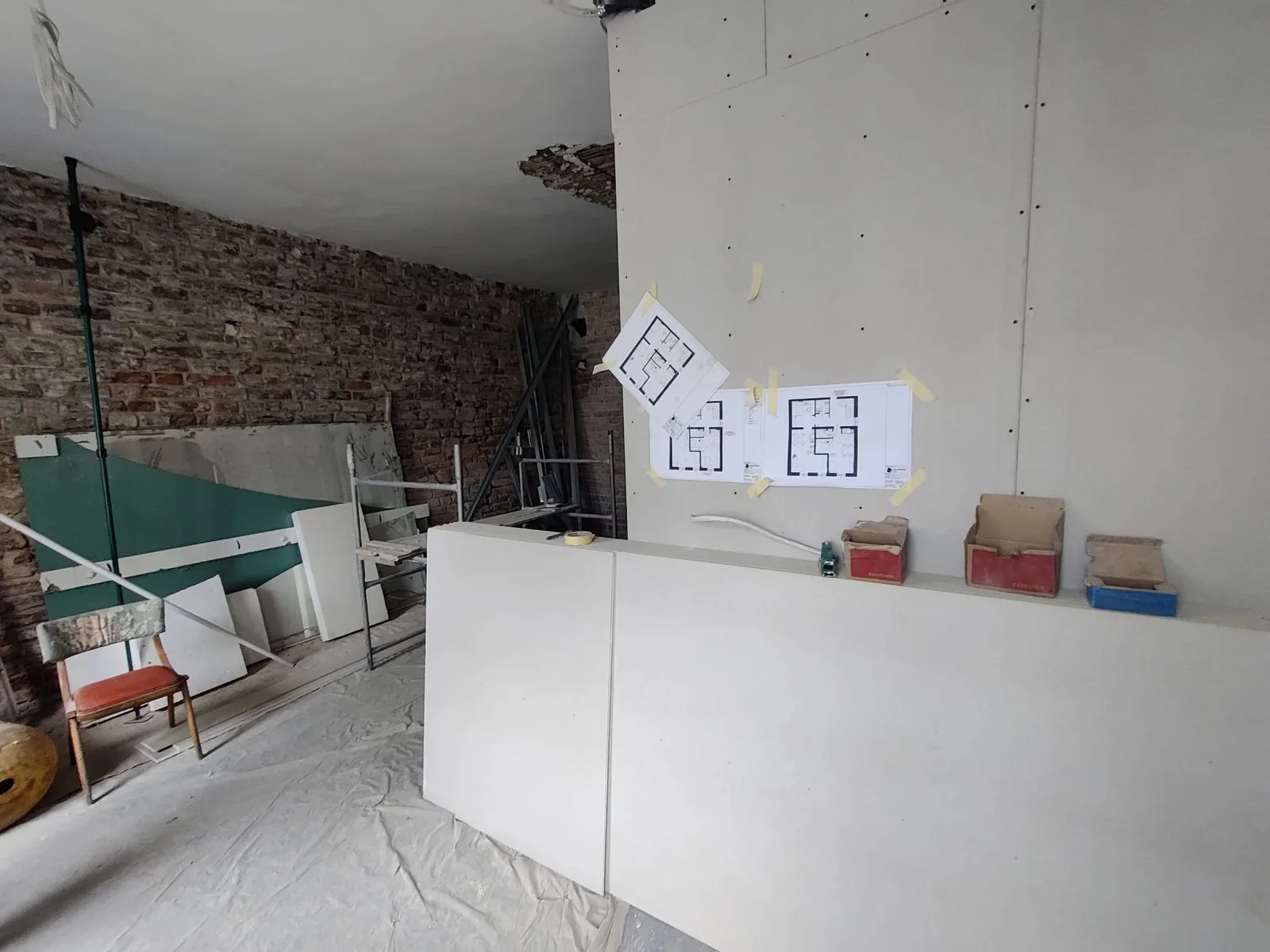 Construction: new partition walls roughed in with exposed timber structure above, construction drawings taped to wall, and floor leveling in progress
