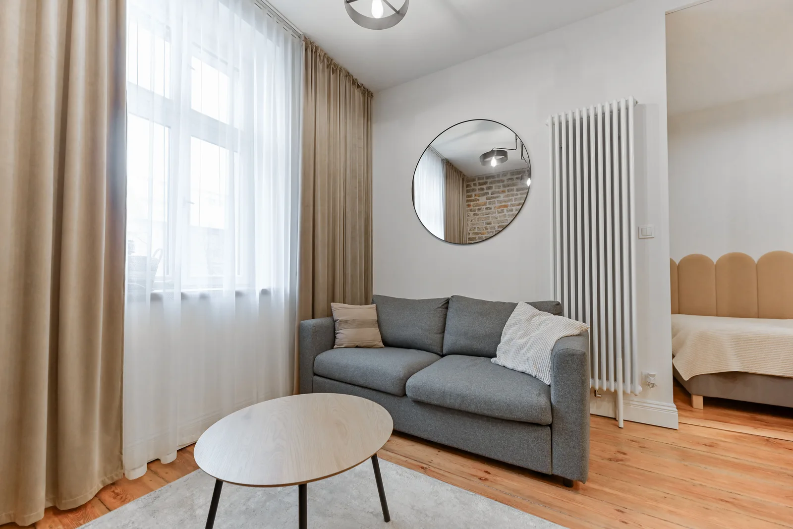Interior: Apartment A living room with TV mounted on timber-clad wall, grey sofa, warm oak flooring, and natural light through heritage windows