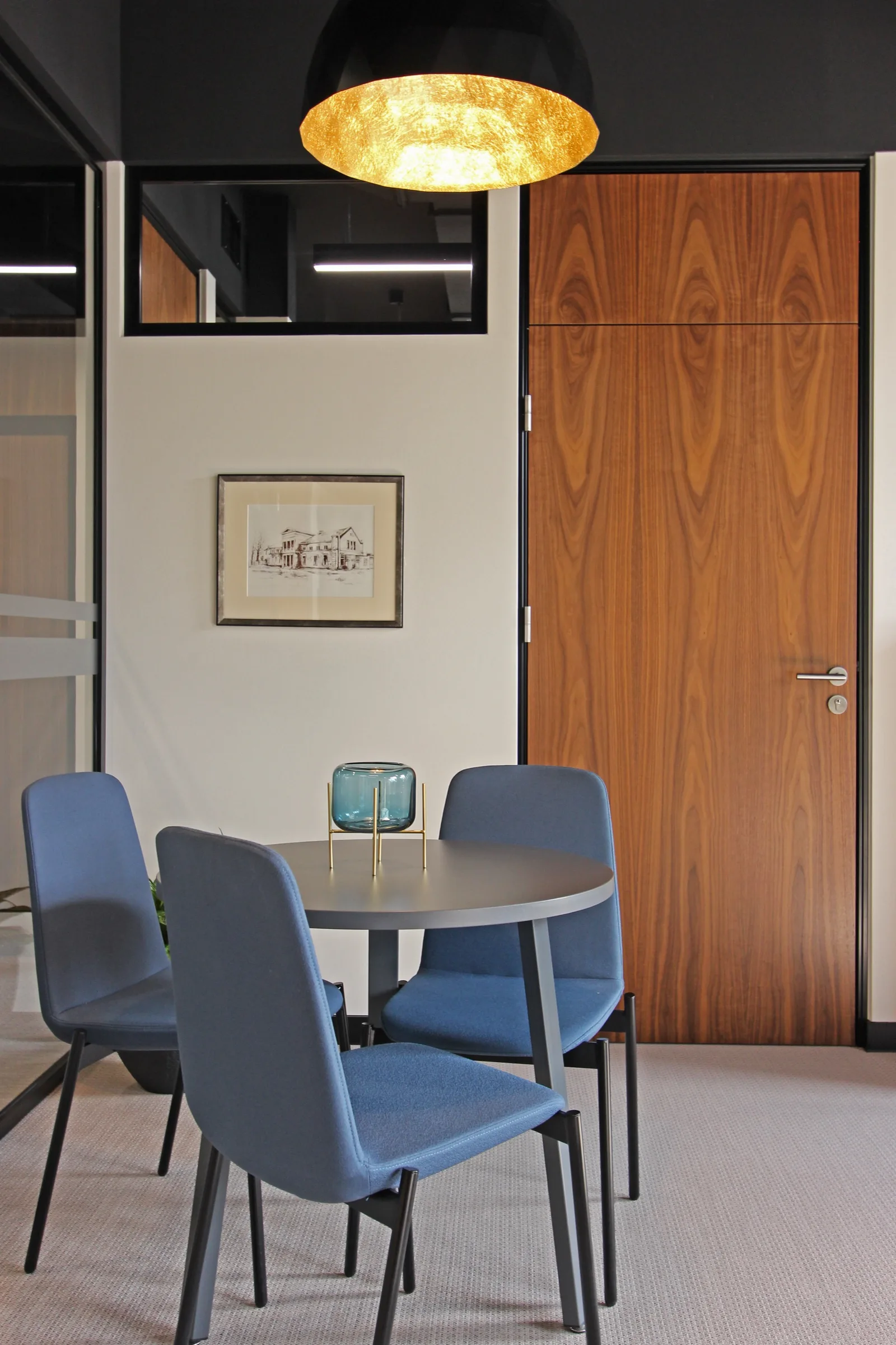 Detail: walnut desk with fabric divider, BenQ monitor, walnut wardrobes behind, and meeting nook visible showing refined corporate workspace materials