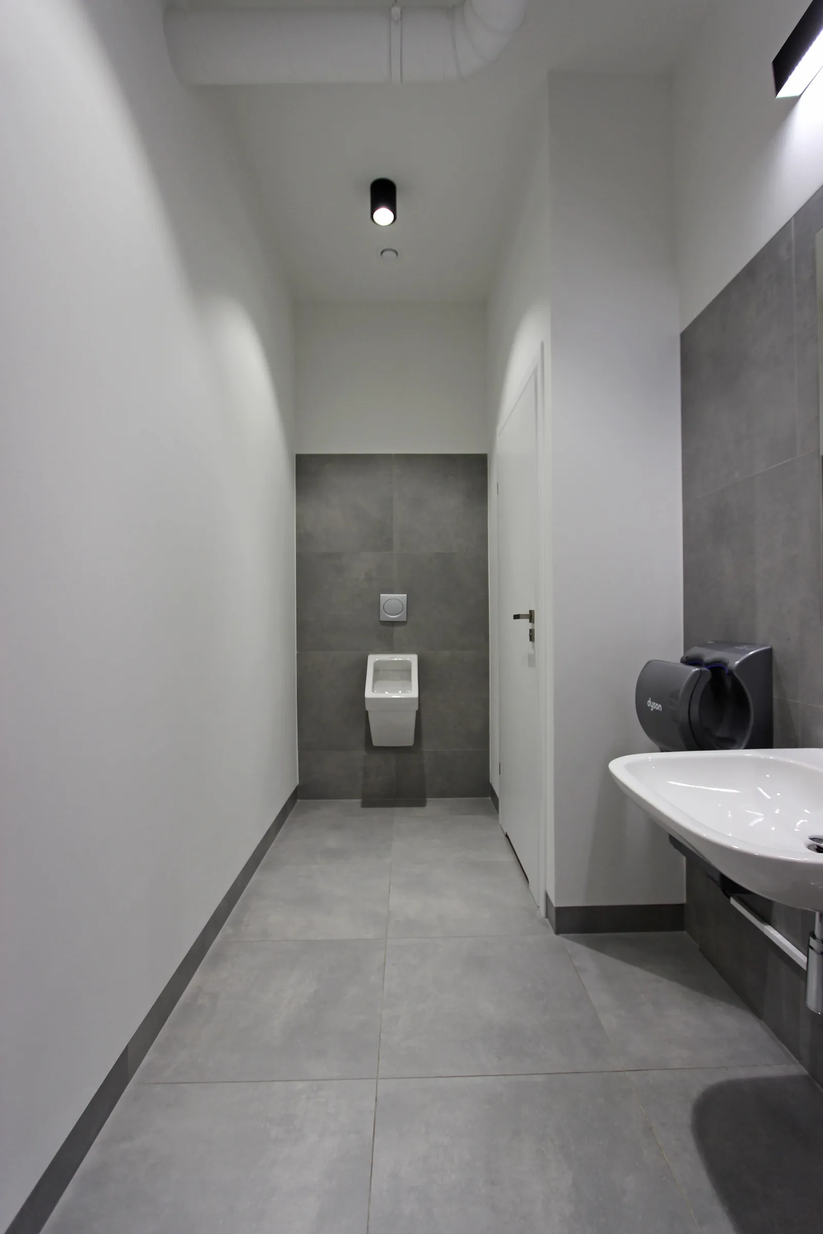 Detail: restroom with large-format grey porcelain tiles, wall-hung WC, wall-mounted basin, and hand dryer