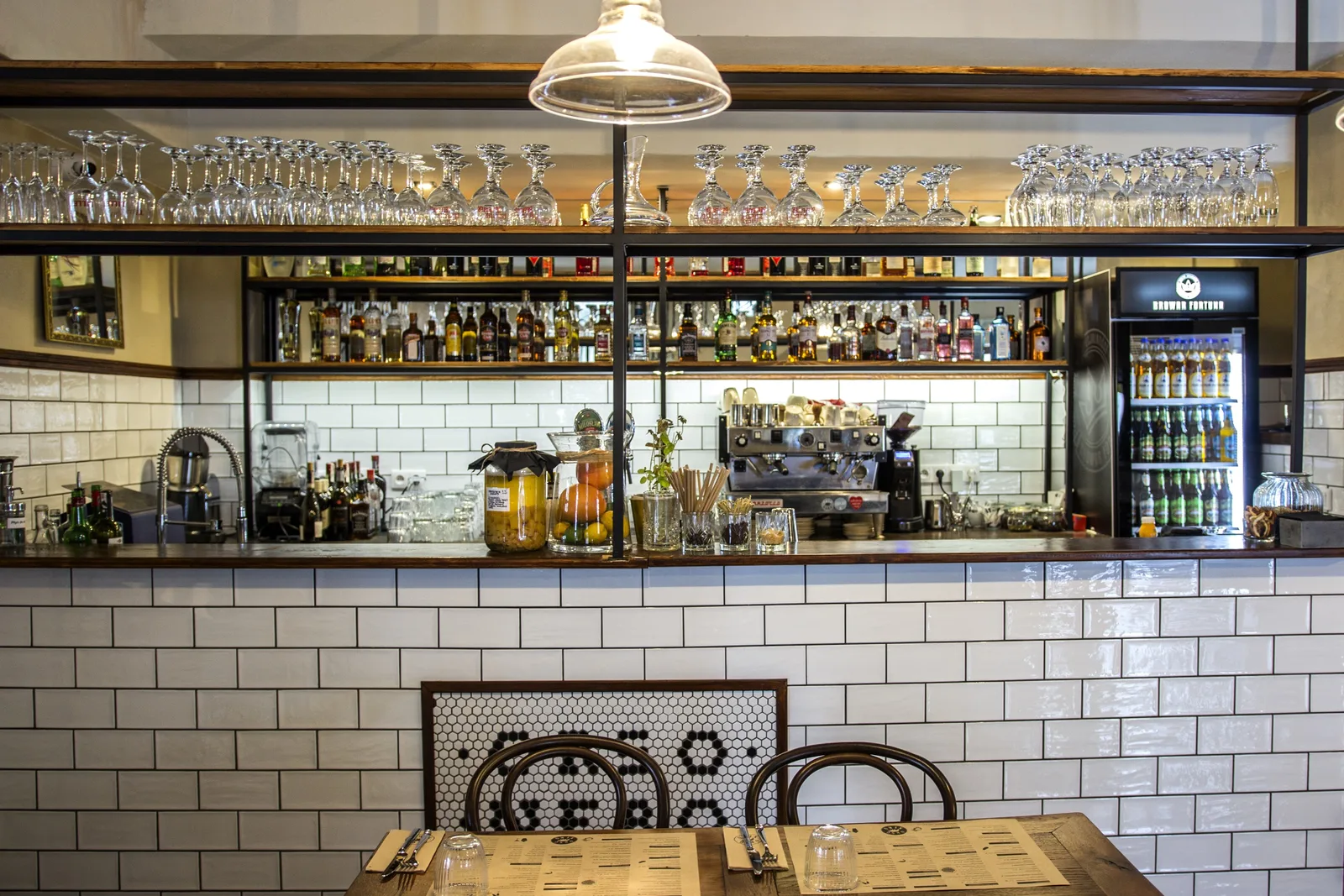 Ground floor dining with Chesterfield leather banquette, bentwood chairs, vintage Italian poster wall, and pendant lighting in warm setting