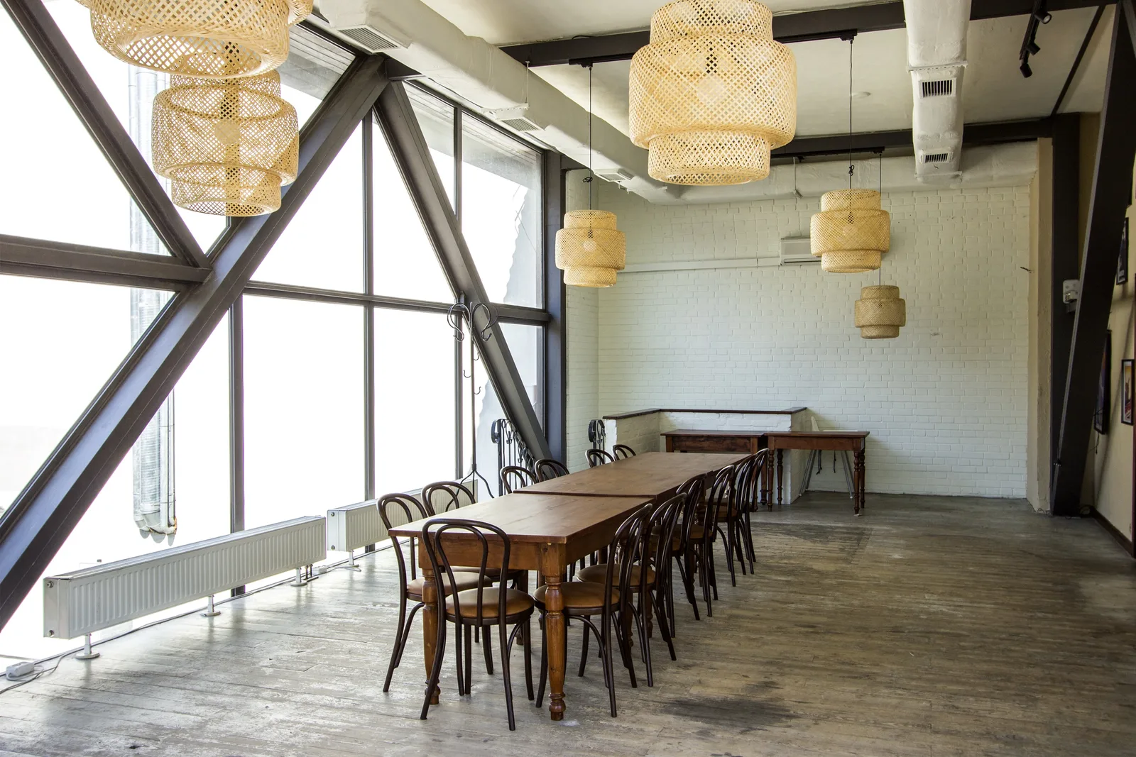 First floor dining with Sinnerlig rattan pendants, triangular steel-framed windows, communal table, reclaimed timber floor, and whitewashed brick walls
