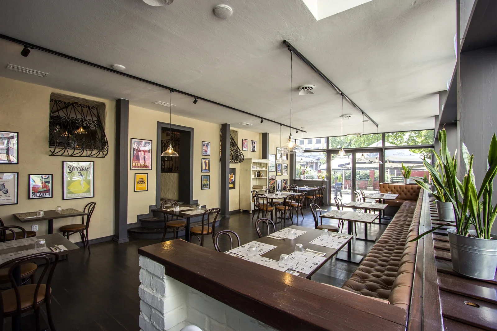 Ground floor dining room with Chesterfield banquette along the window wall, bentwood chairs at vintage tables, and Italian poster gallery above