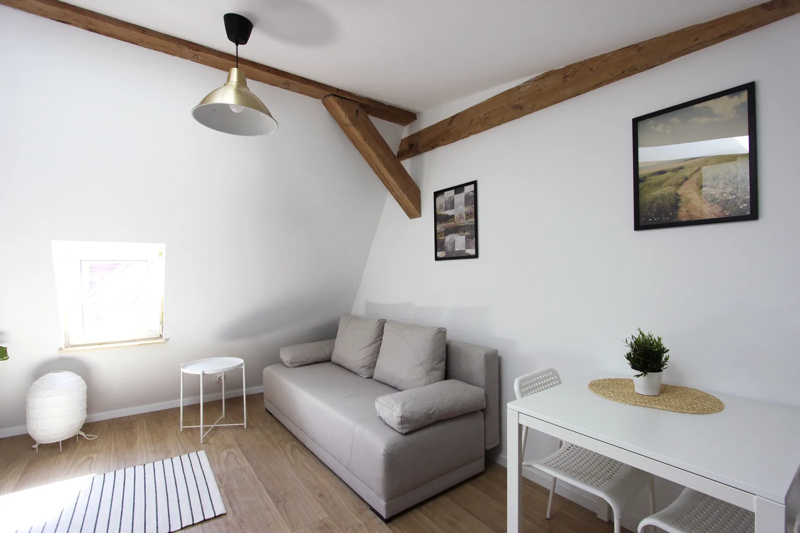 Interior: living room with exposed timber cross-brace beam, paper lantern pendant lighting, white walls amplifying natural daylight, and warm Scandinavian-minimalist aesthetic across all eight units