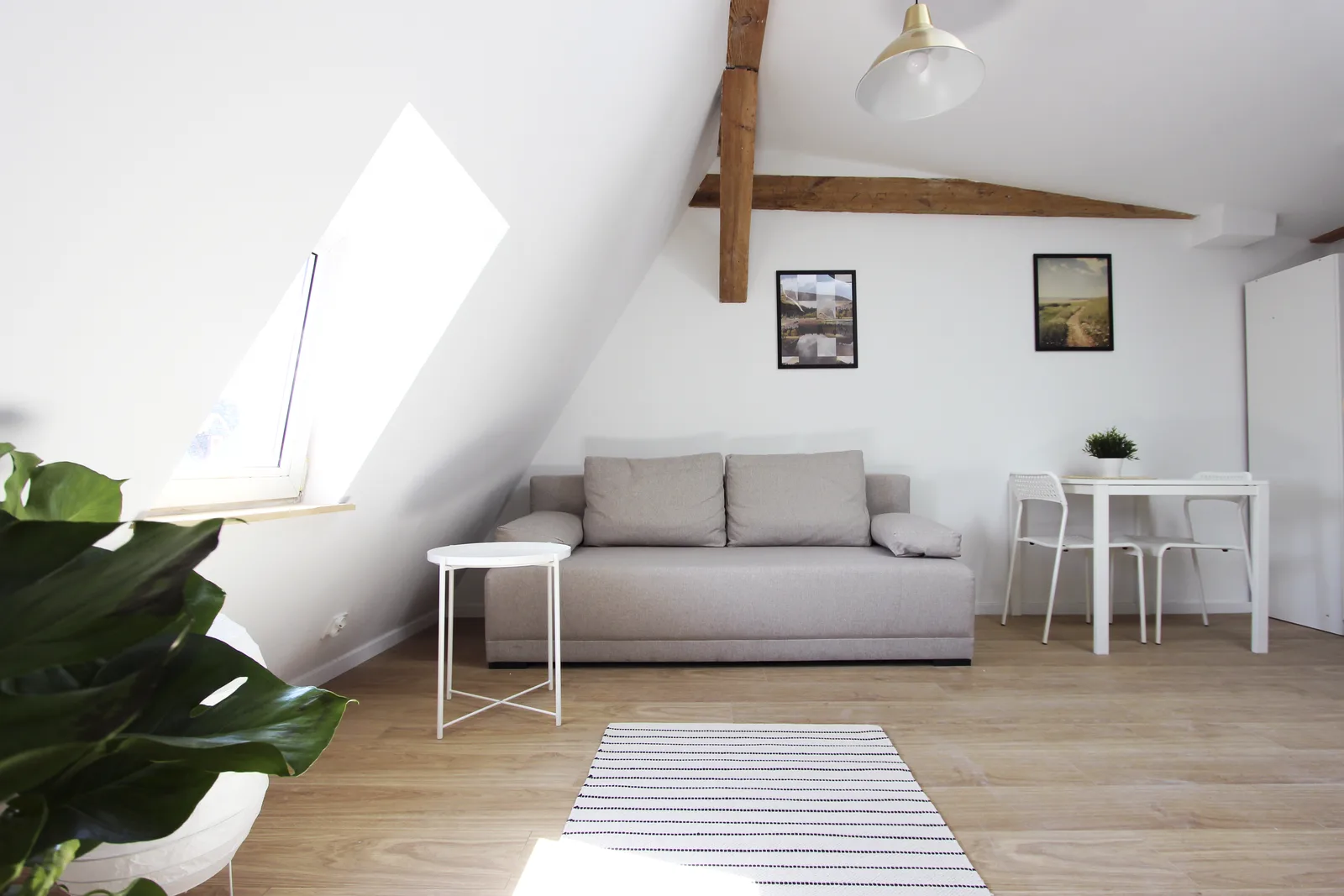 Interior: navy futon seating arrangement beneath gable windows with exposed aged timber beams overhead, demonstrating controlled variation between the eight attic apartment unit designs