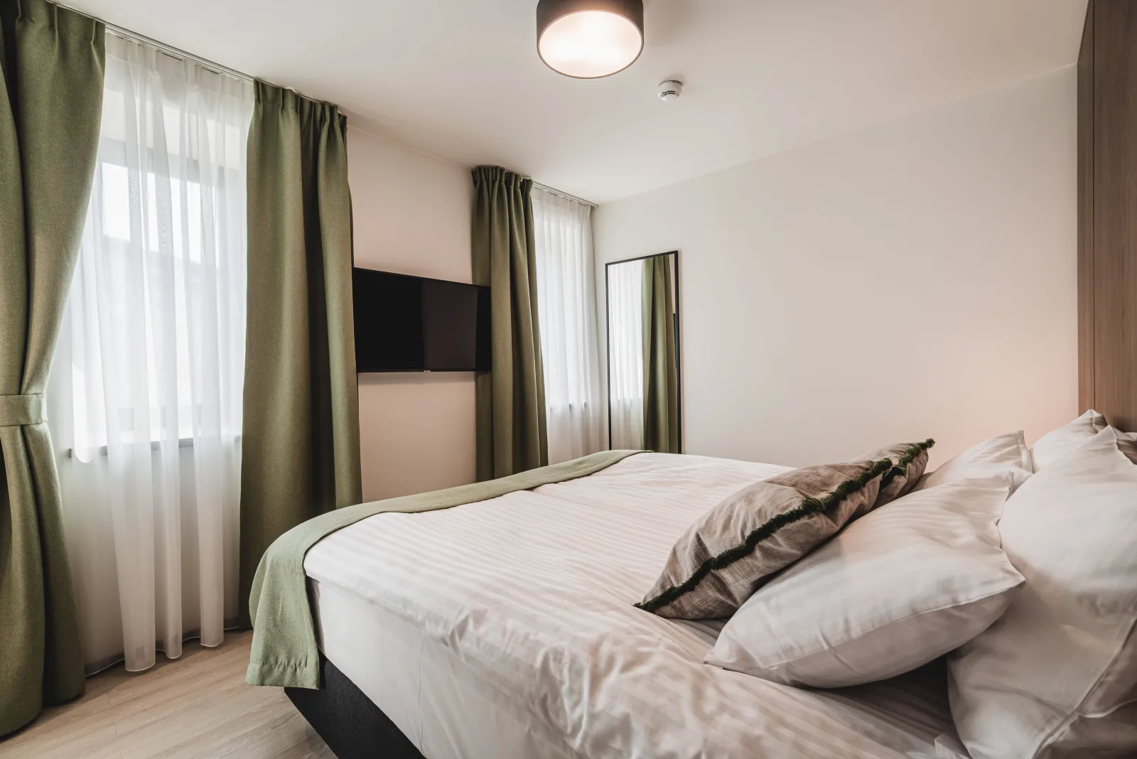 Bedroom with green bedspread, cushions, art above bed