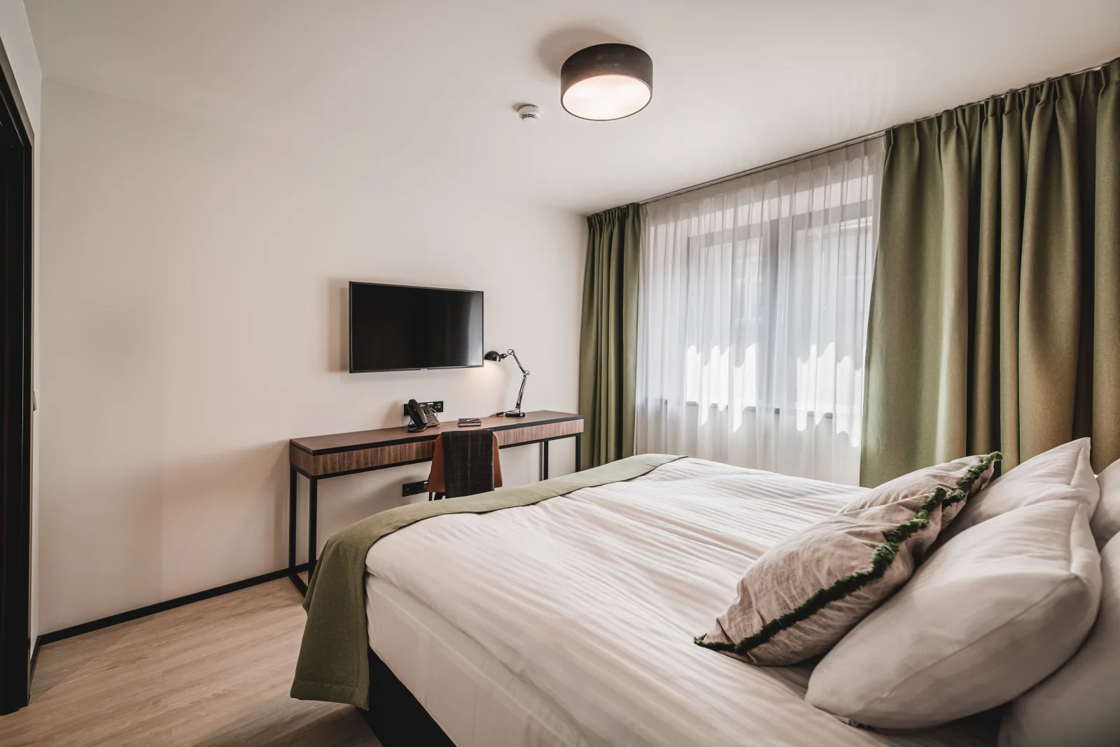 Bedroom with white bedding, green curtains, desk lamp