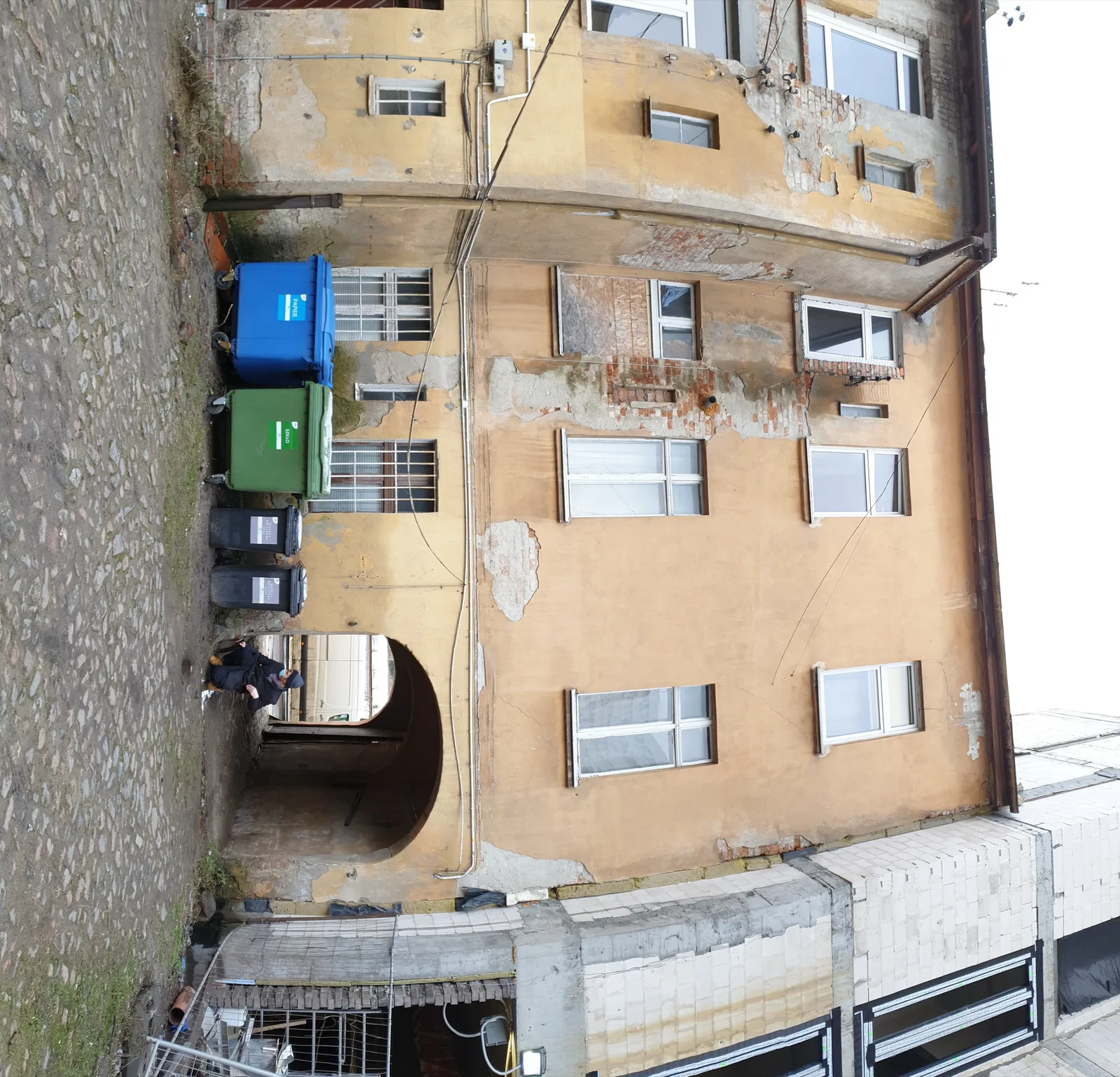 Before: courtyard view of ochre heritage facade with original wooden gate, weathered plaster, and deteriorated rear structure before demolition