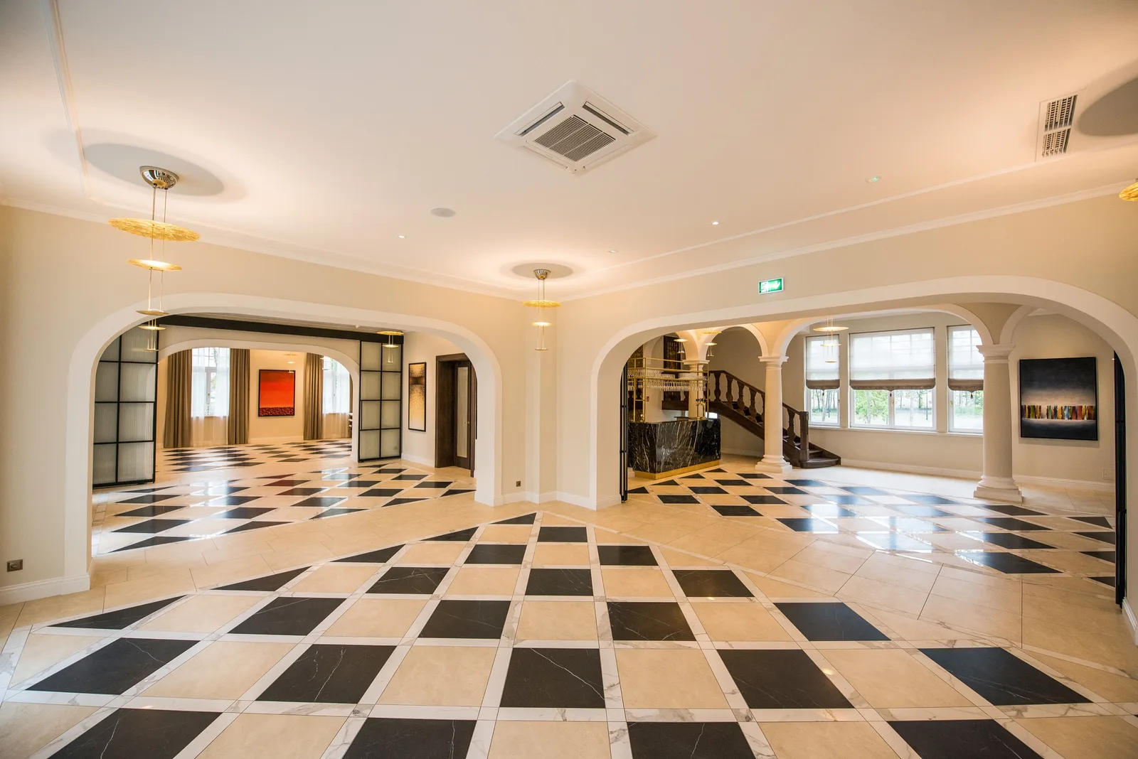 Wide lobby panorama with checkered floor, arches, paintings, and staircase in distance