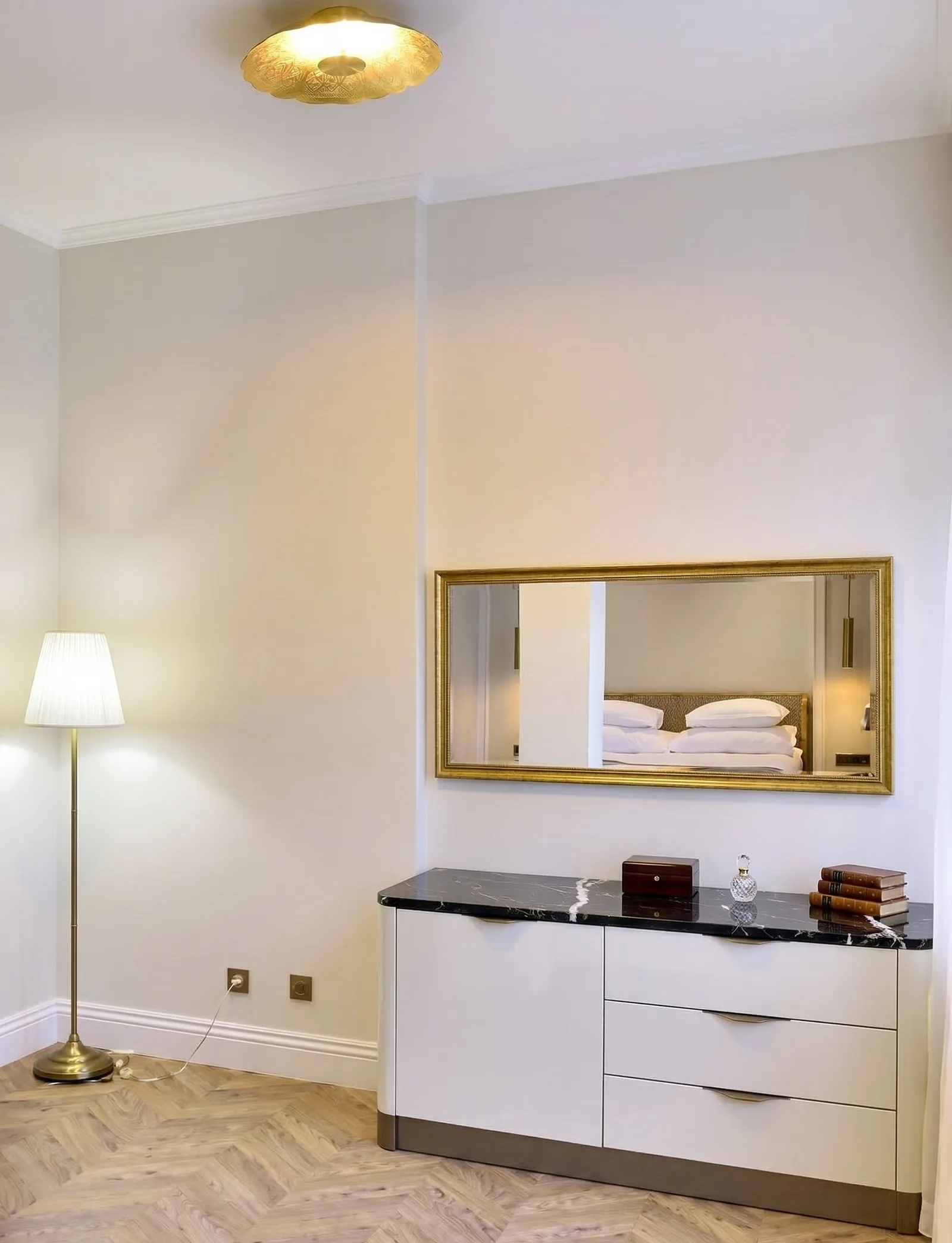 Portrait view of dresser with gold mirror, ceiling light, lamp, and herringbone floor — Gemini upscale