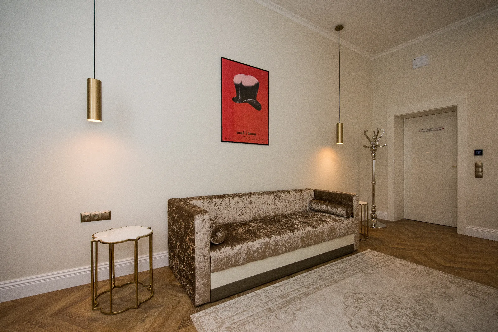 Hotel room sitting area with red poster art, velvet sofa, and pendant lighting