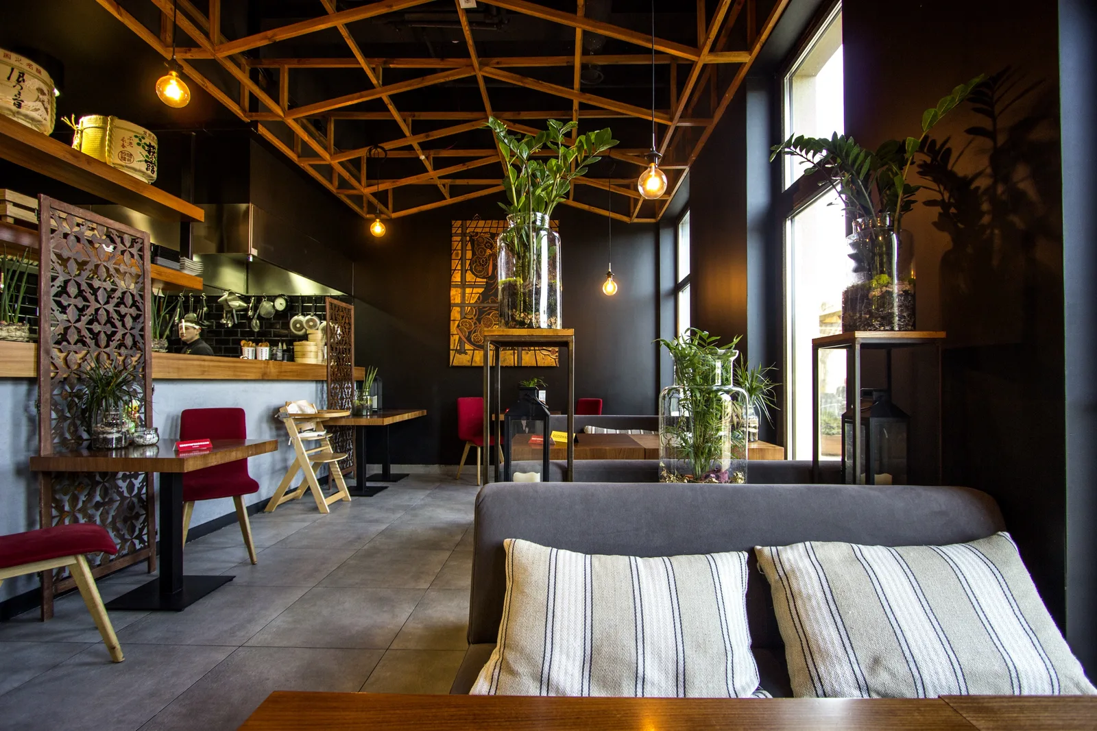 Interior: main dining floor from window side, bar left, sofa and striped cushions foreground, evening mood