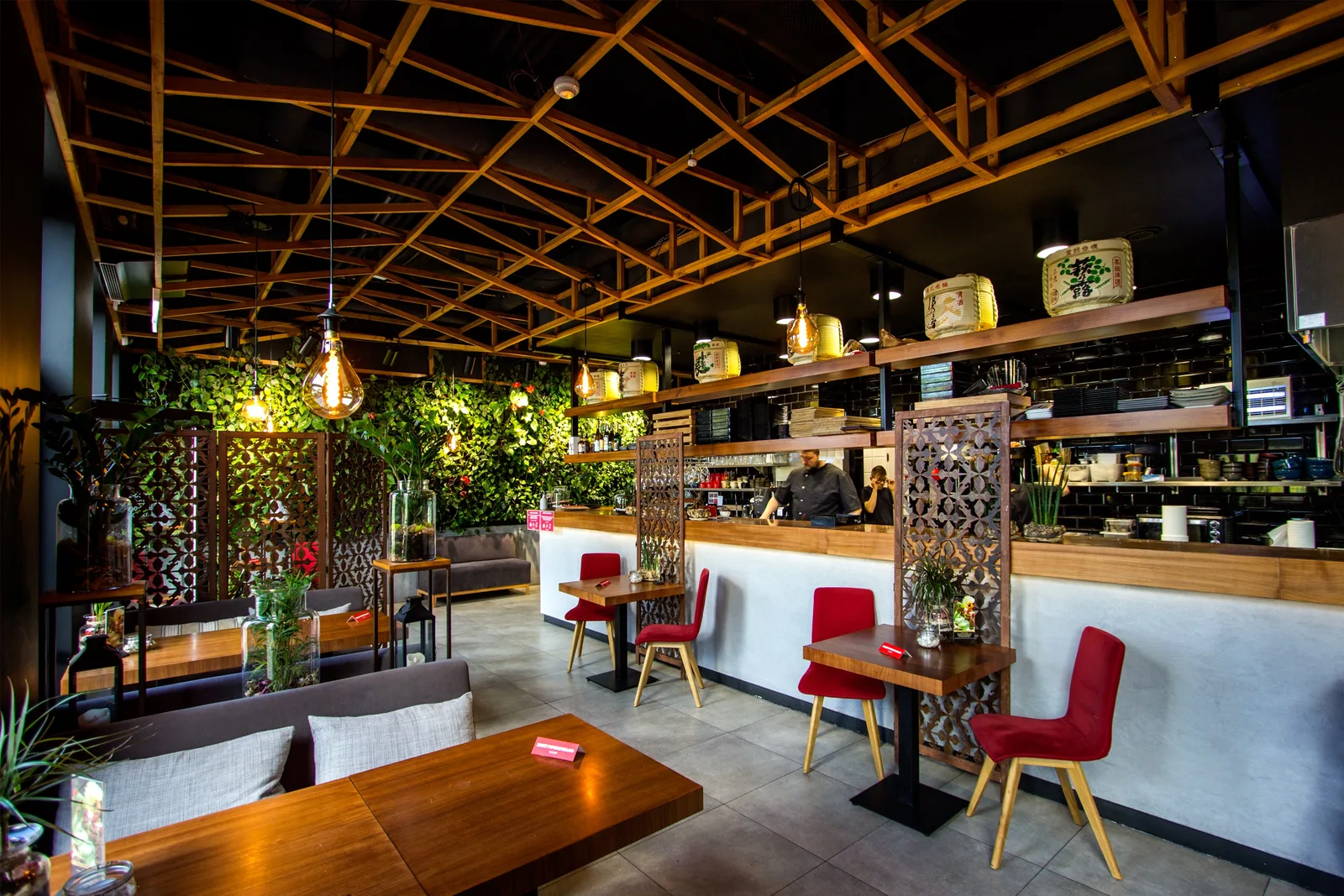 Interior: bar area with staff — chef at work, full bar counter, sake barrels, dining area visible